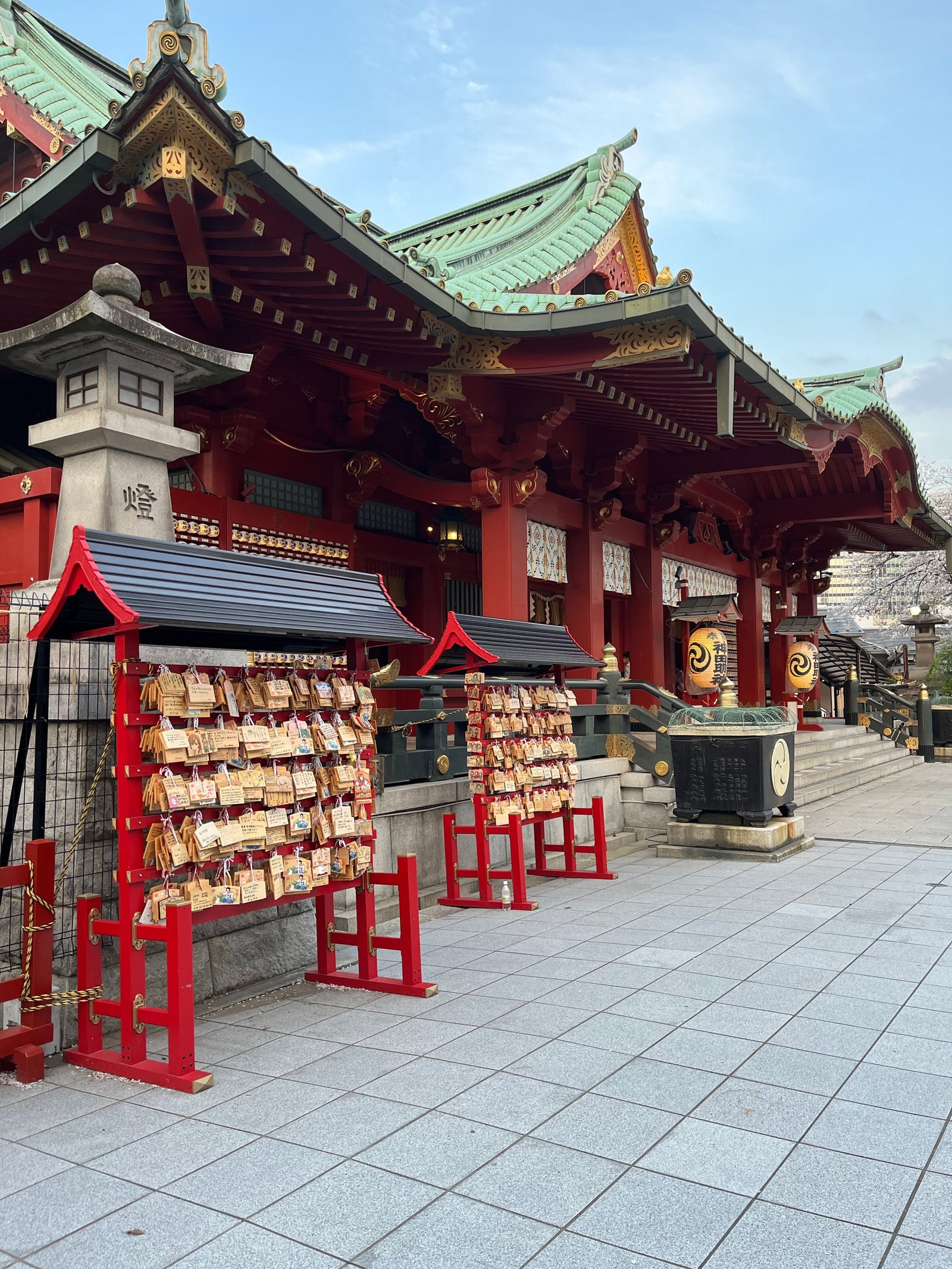 The red shrine hall at Kanda Myojin with racks of wooden ema plaques and a stone lantern