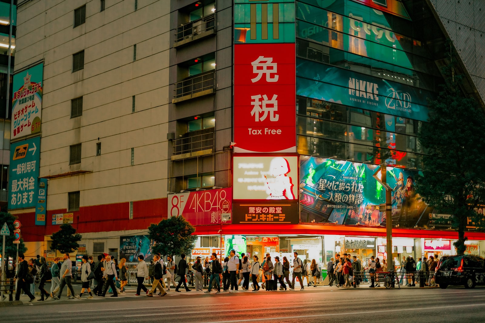A corner of Akihabara at night with lit shop signs and people crossing the road