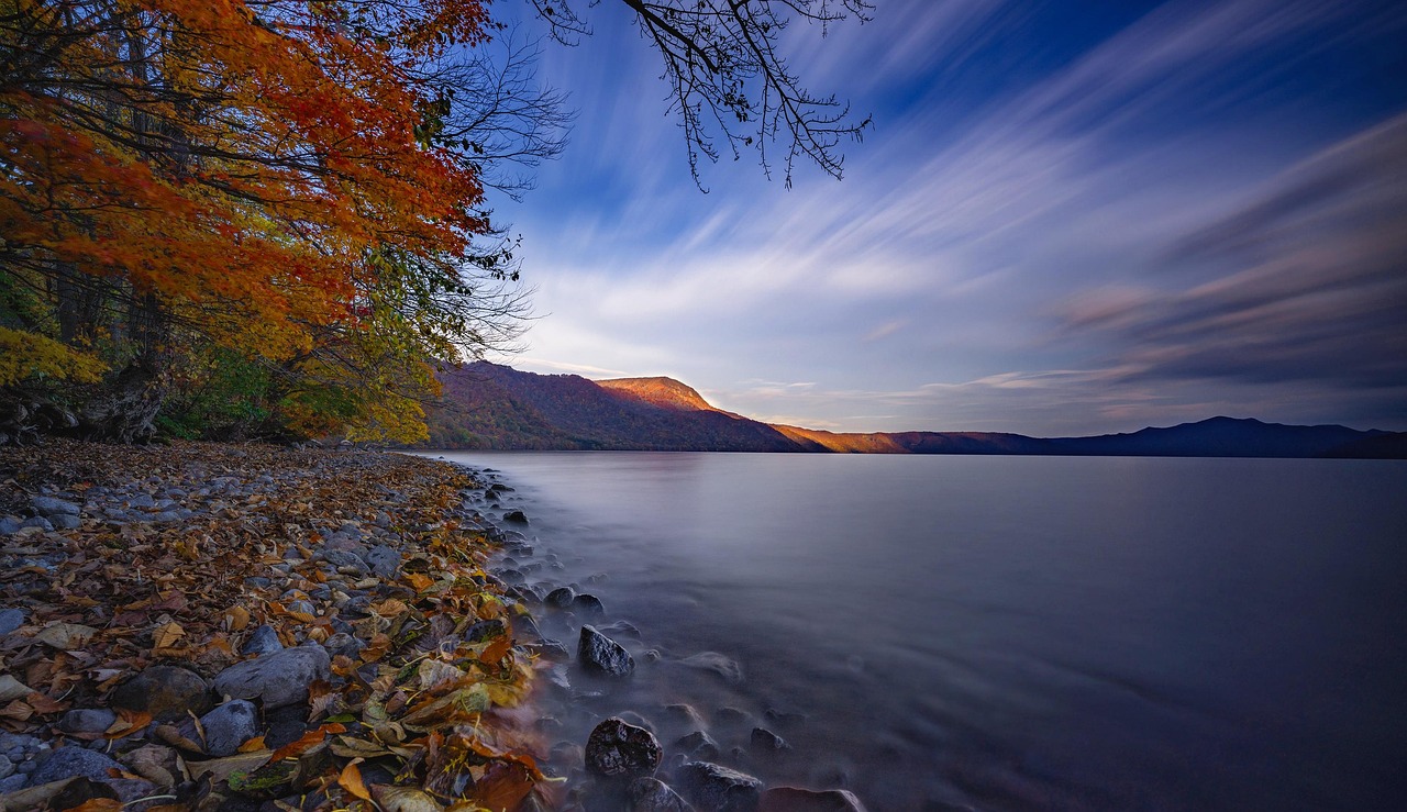 The shore of Lake Towada in autumn, red trees over the water