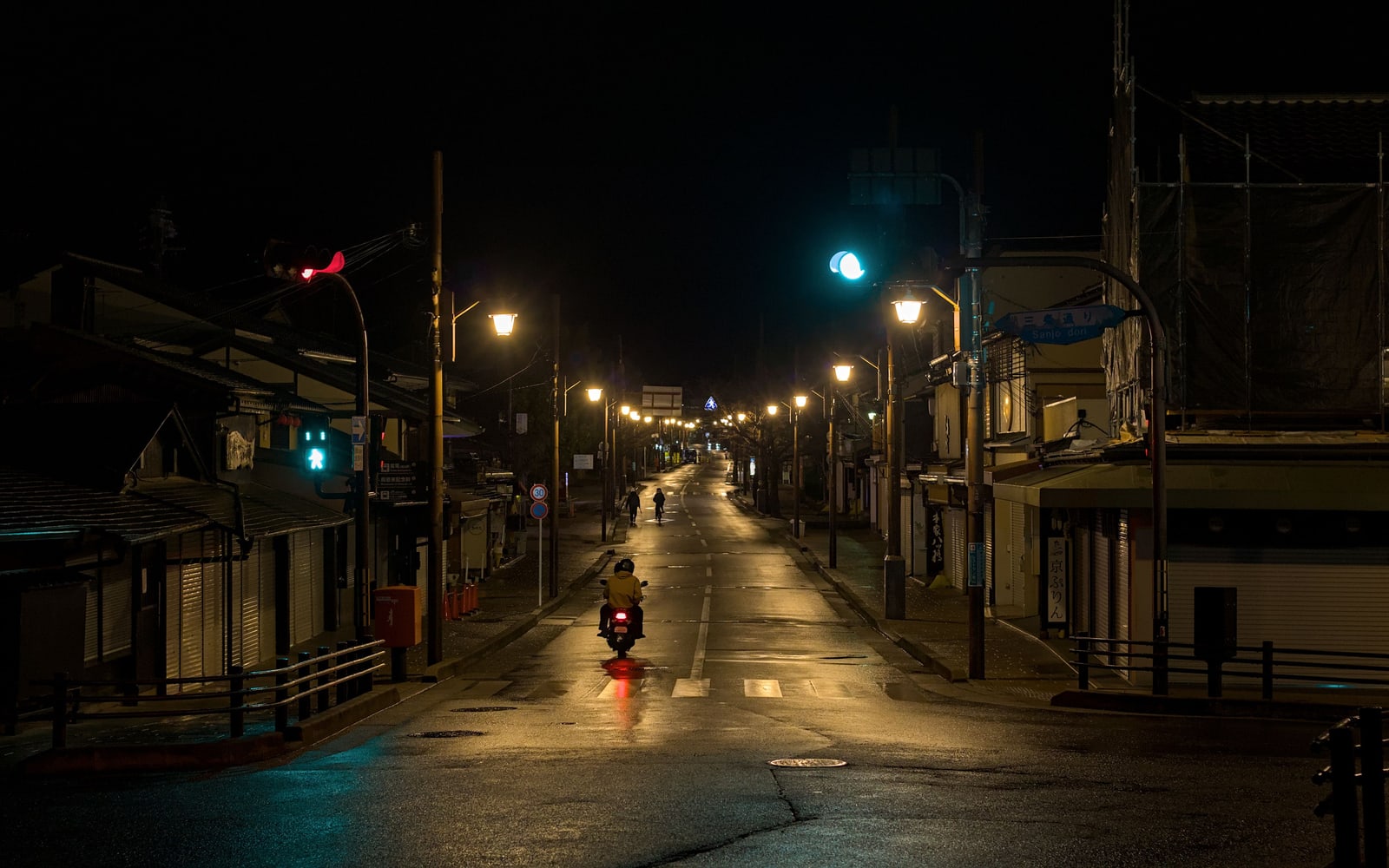 An empty street in Arashiyama at night, wooden houses lit by streetlights, one motorbike far down the road.