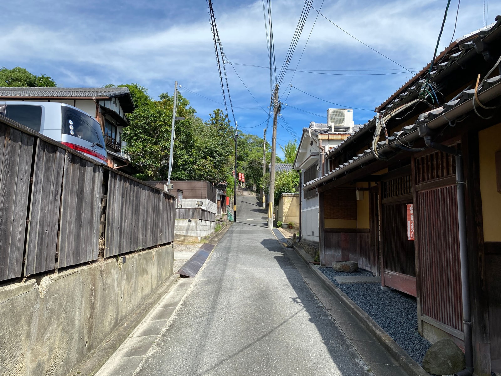 A narrow empty residential lane in Arashiyama with wooden houses and a timber fence under a blue sky.