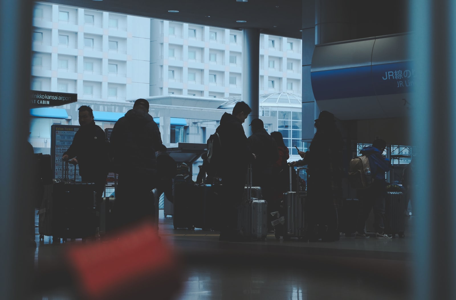 Silhouetted travelers with suitcases queuing by a JR Lines entrance at Kansai Airport station.