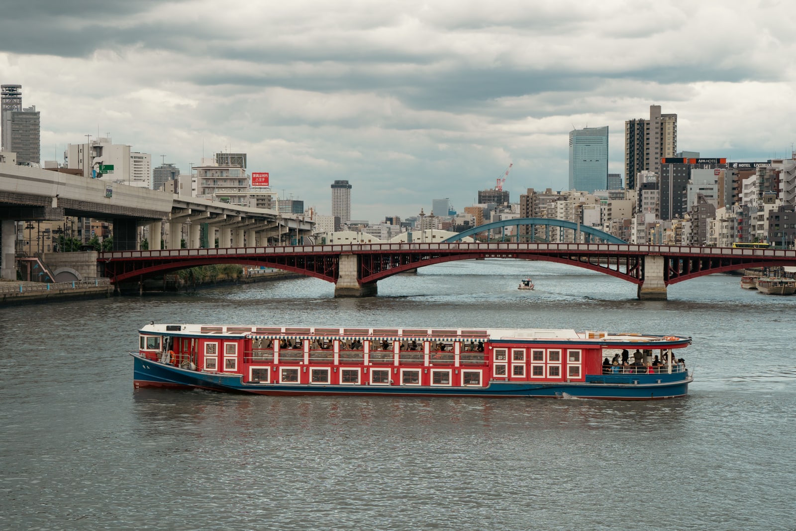 A red-and-blue passenger boat on the Sumida River in front of a red steel arch bridge
