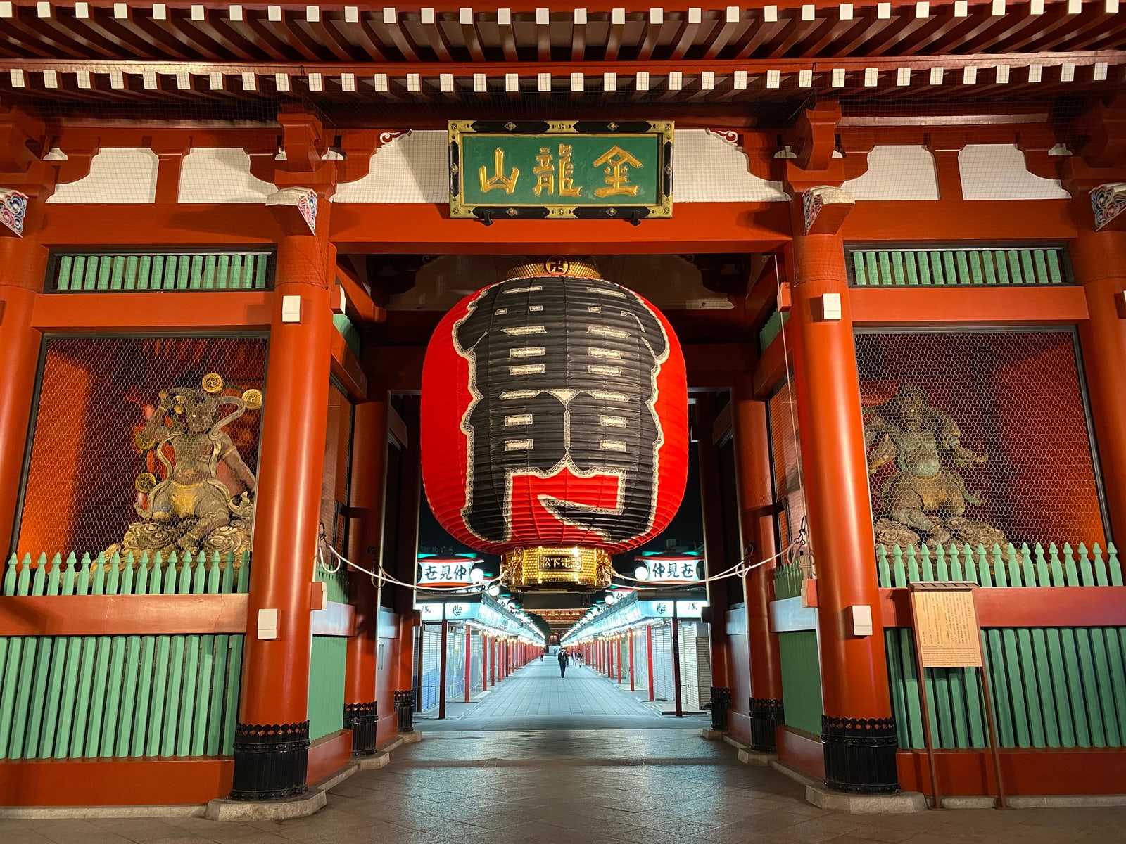 The Kaminarimon at night, a large red lantern hanging between two guardian statues, with the Nakamise arcade empty and shuttered beyond