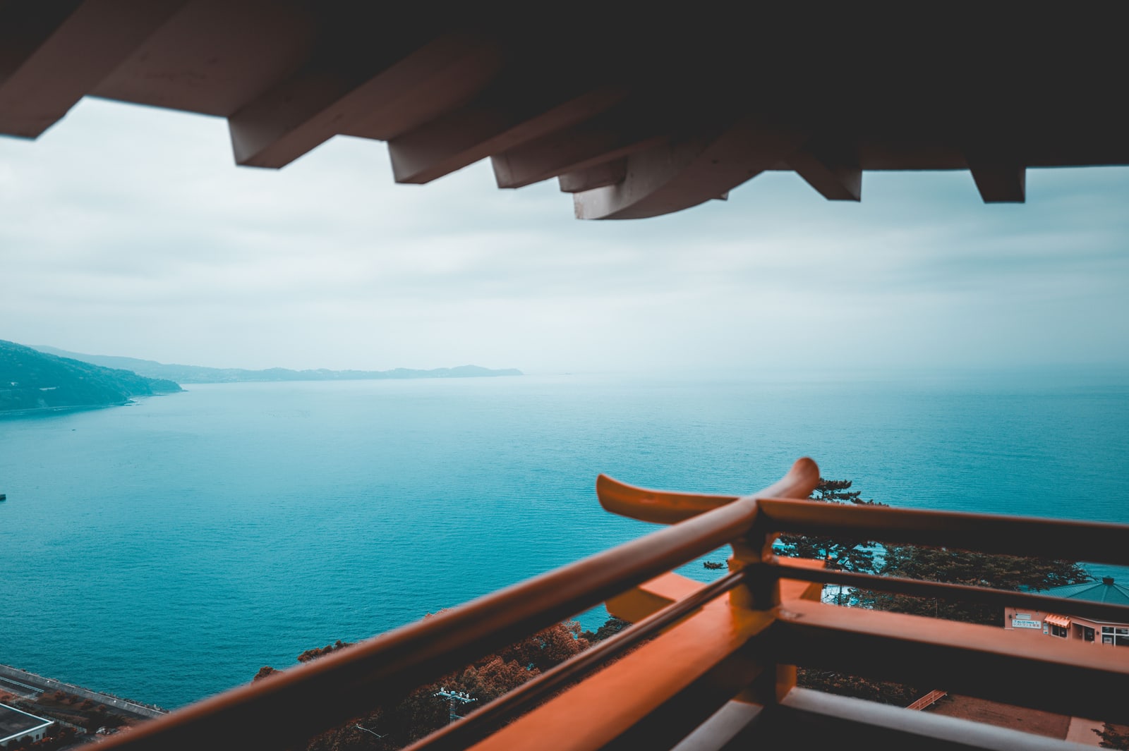 The sea off Atami seen from a high balcony under traditional wooden eaves, an orange-red railing in front