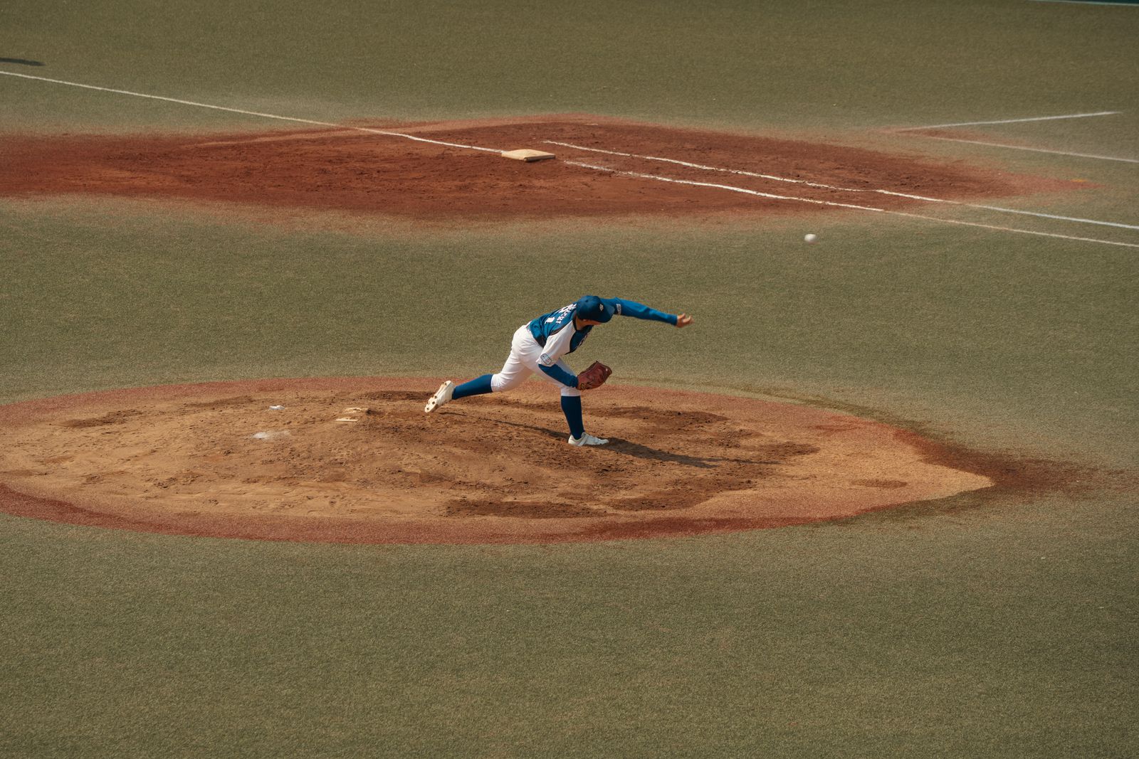 A pitcher on the mound at full follow-through, the ball just released, on an artificial-turf field.