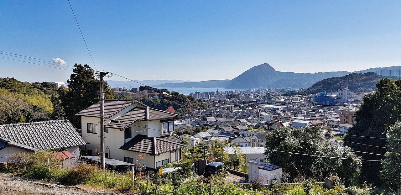 Houses running down a hillside to a bay, a cone-shaped mountain across the water under a clear sky