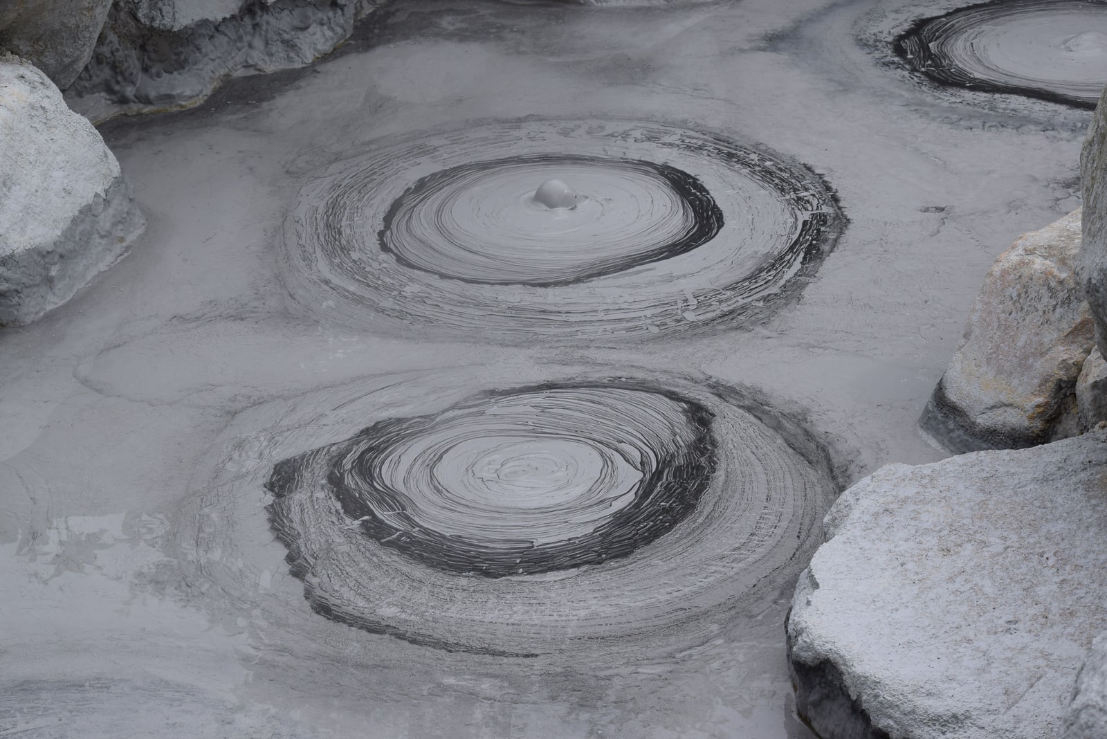 Bubbling grey mud forming concentric rings between pale rocks