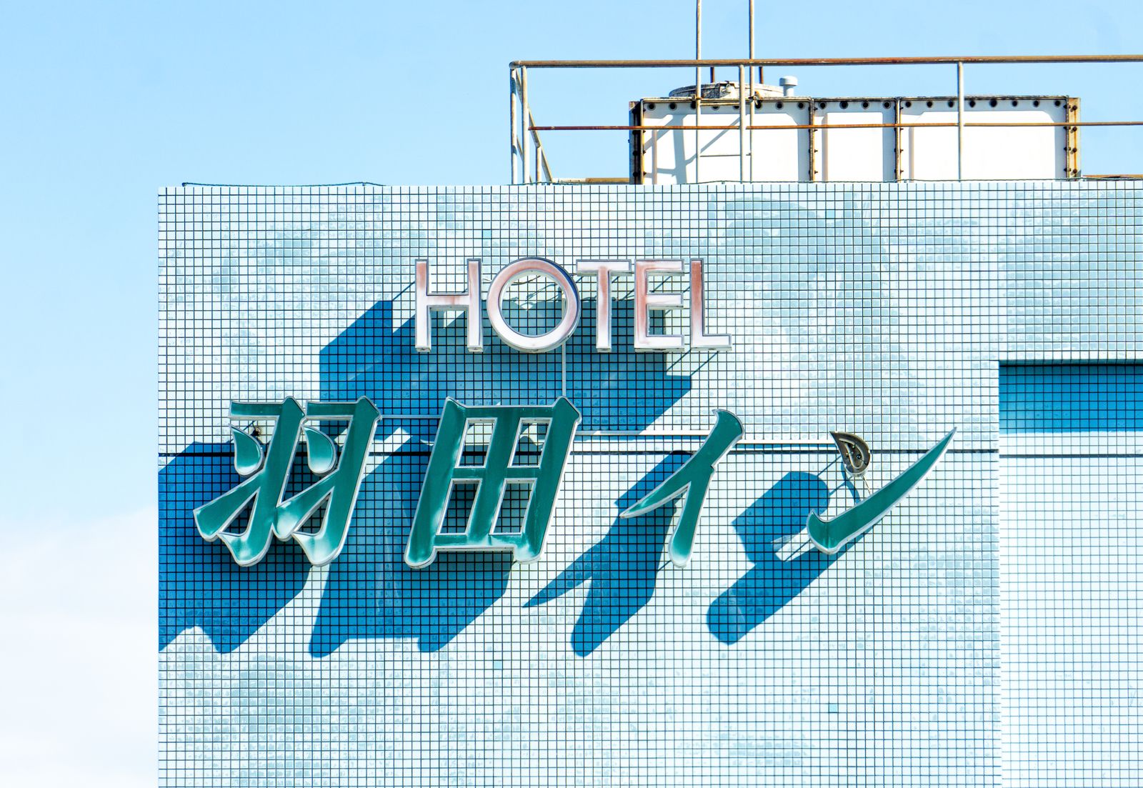 A plain HOTEL sign on a blue-tiled building under a clear sky, Tokyo.