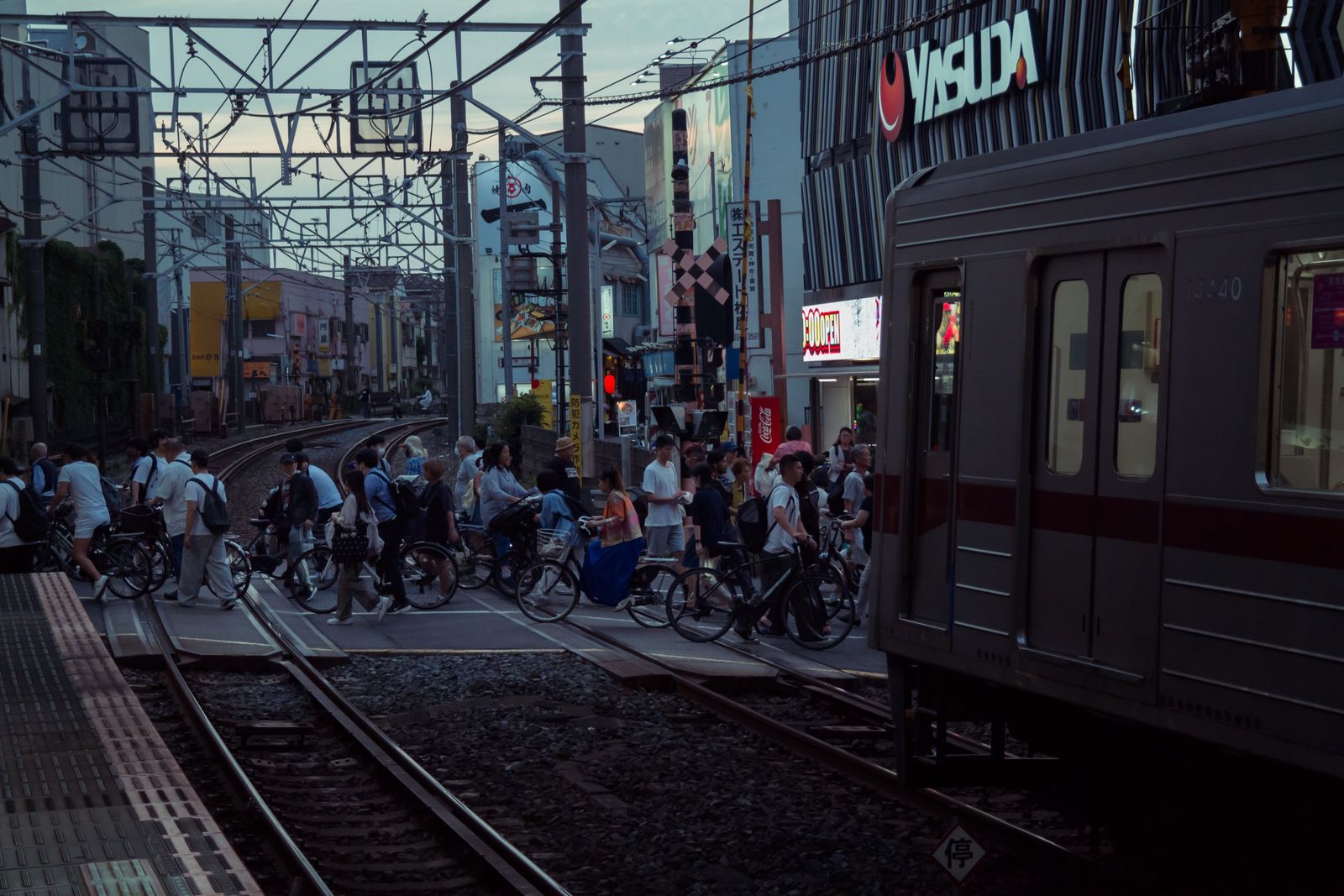 Commuters and cyclists pour across a railway level crossing at dusk as a train passes, Tokyo.