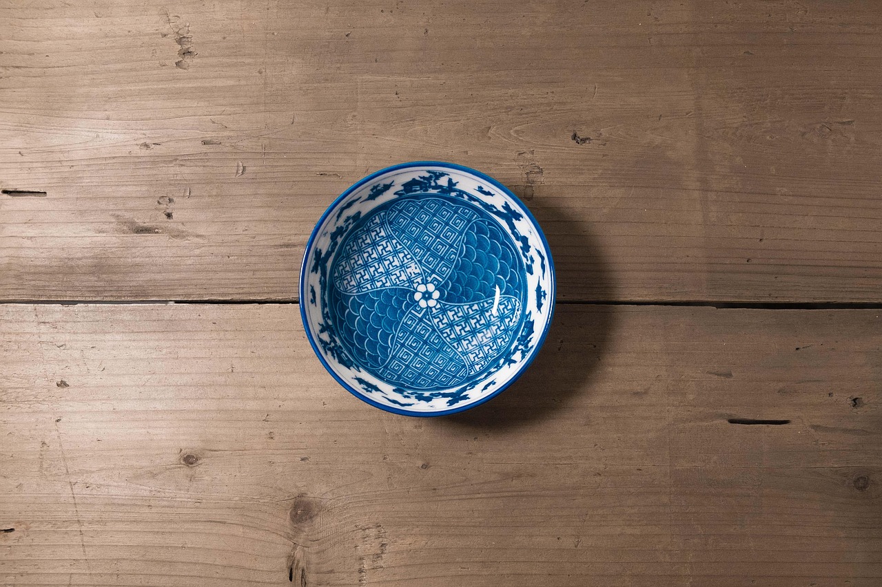 A glazed white-and-tan ceramic bowl sitting on a matching plate, with chopsticks and a sprig of dried flowers, plain background.