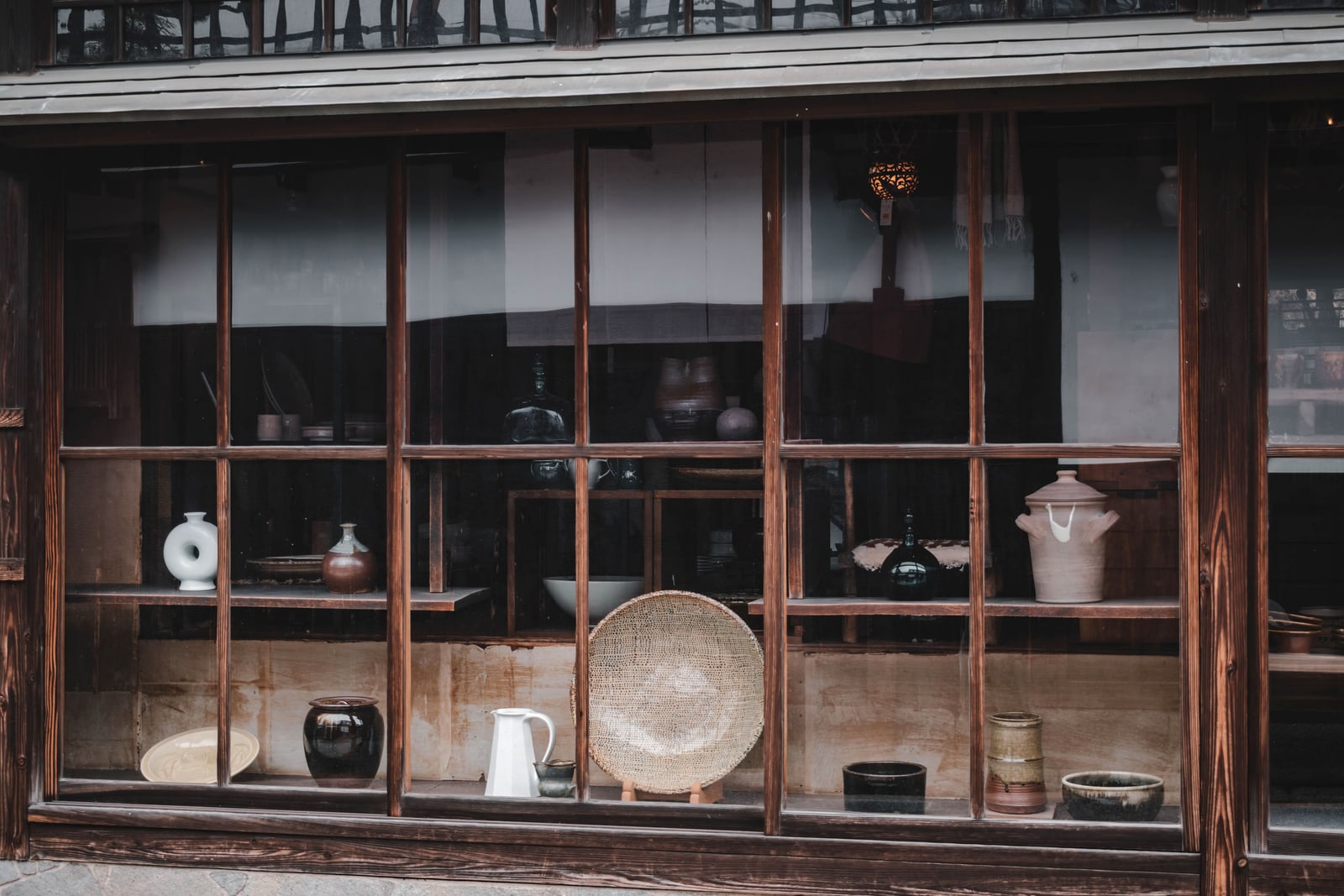 A traditional wood-framed shopfront window in Kurashiki, Okayama, displaying vases, bowls and jars on shelves.