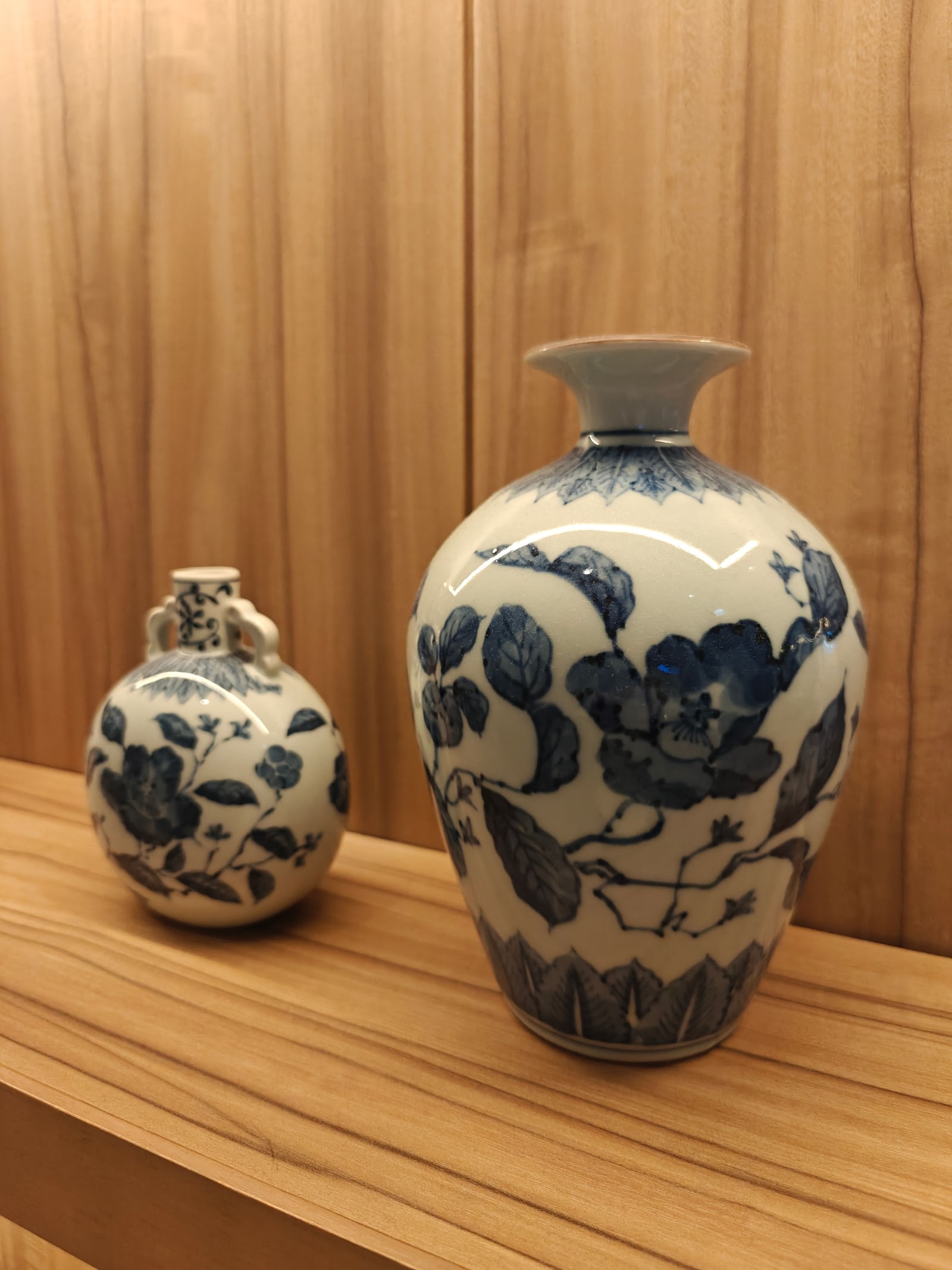 Two blue-and-white porcelain vases with floral painted decoration on a wooden shelf.