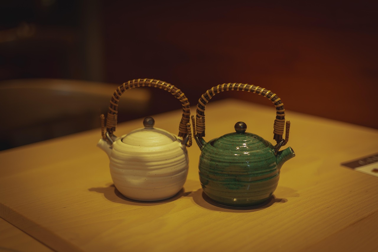 Two round earthenware teapots with bamboo-wrapped handles, one white-glazed and one green-glazed, on a wooden table.
