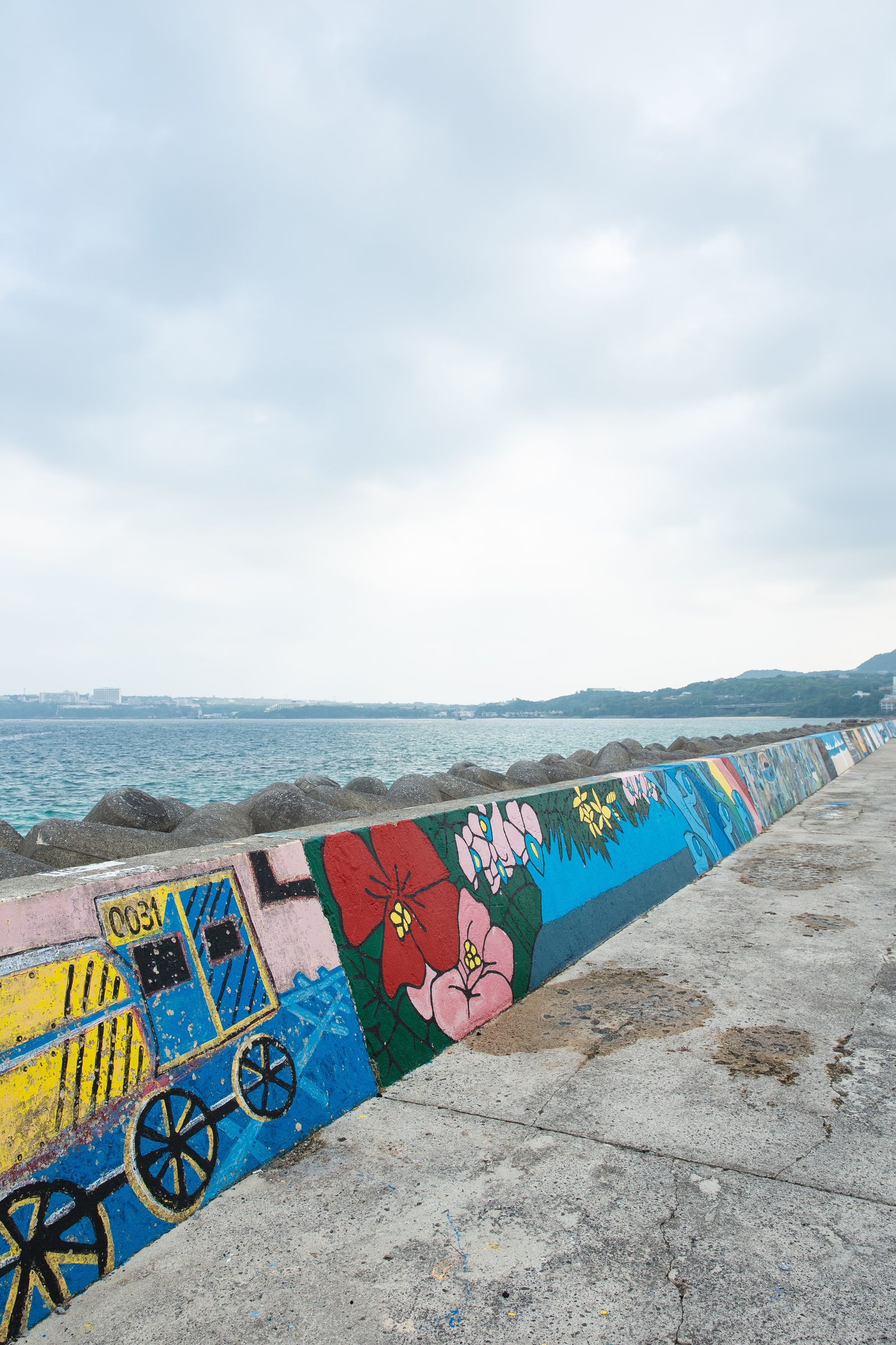 A painted seawall and walkway beside a turquoise sea under an overcast sky