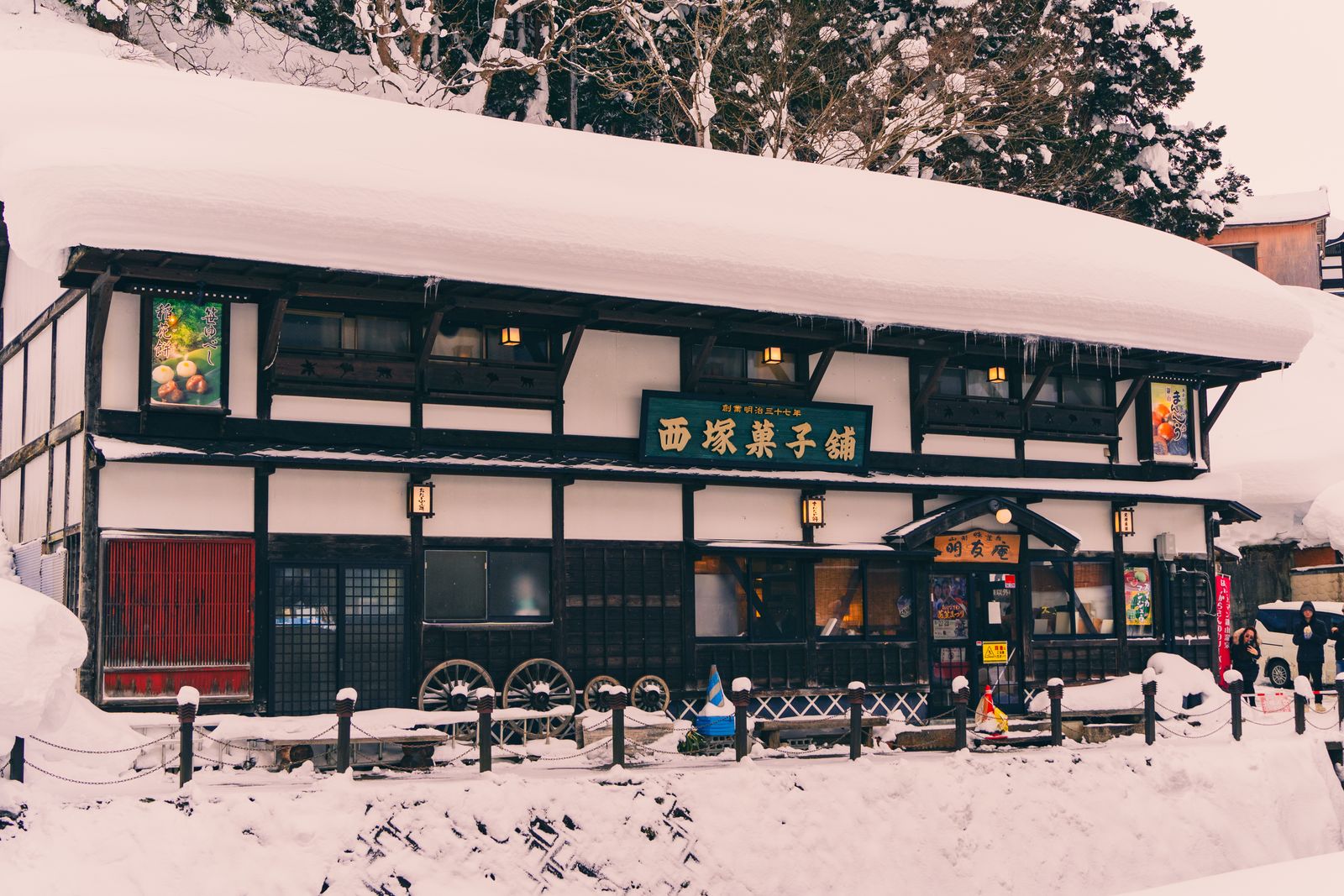 A century-old Japanese confectionery shop open for business under a meter of roof snow, lanterns lit.