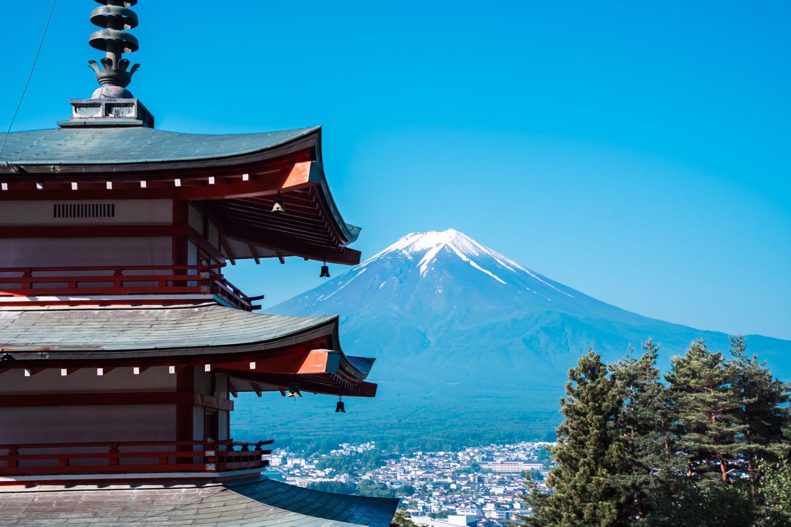 The red eaves of the Chureito pagoda at left, Mount Fuji in the center and the town of Fujiyoshida below, under a clear sky.