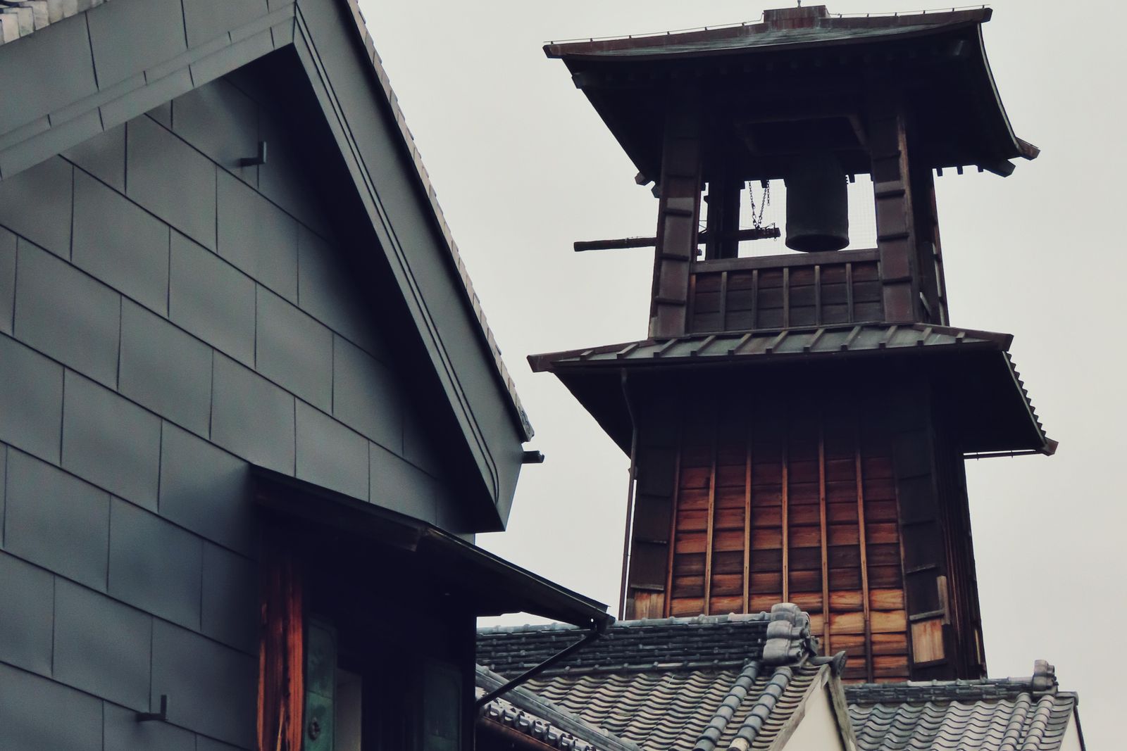The wooden Toki no Kane bell tower rising behind tiled kurazukuri roofs in Kawagoe, under an overcast sky.