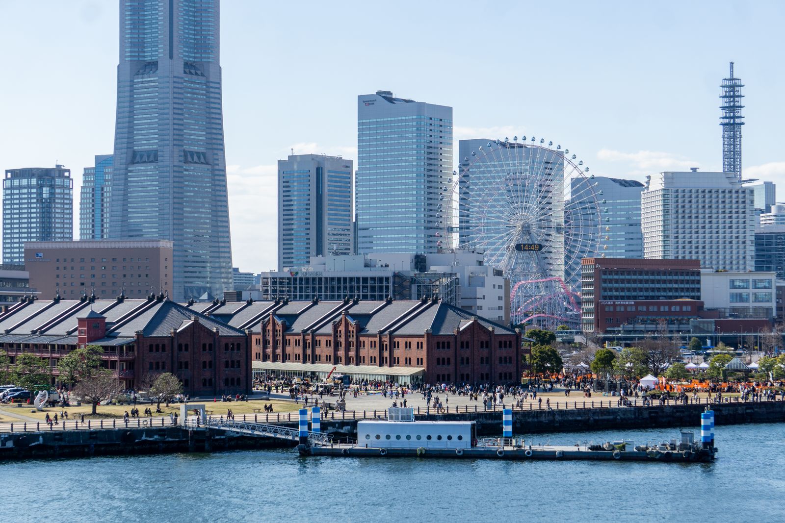 The Yokohama Red Brick Warehouses seen from the water, a crowd on the quay and the Cosmo Clock 21 wheel and Landmark Tower behind