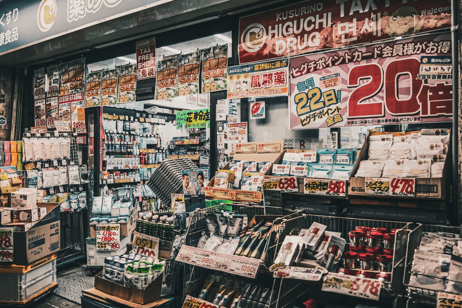 A densely stocked Japanese drugstore shopfront, hung with kusuri, cold-medicine and hay-fever signs and yen price cards.