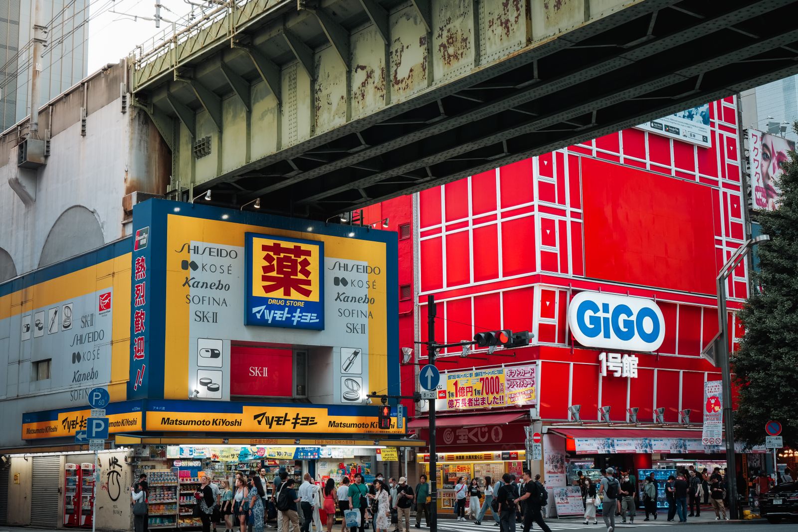 A Matsumoto Kiyoshi under a Tokyo railway overpass in daylight, its facade advertising Shiseido, Kosé, Kanebo, Sofina and SK-II.