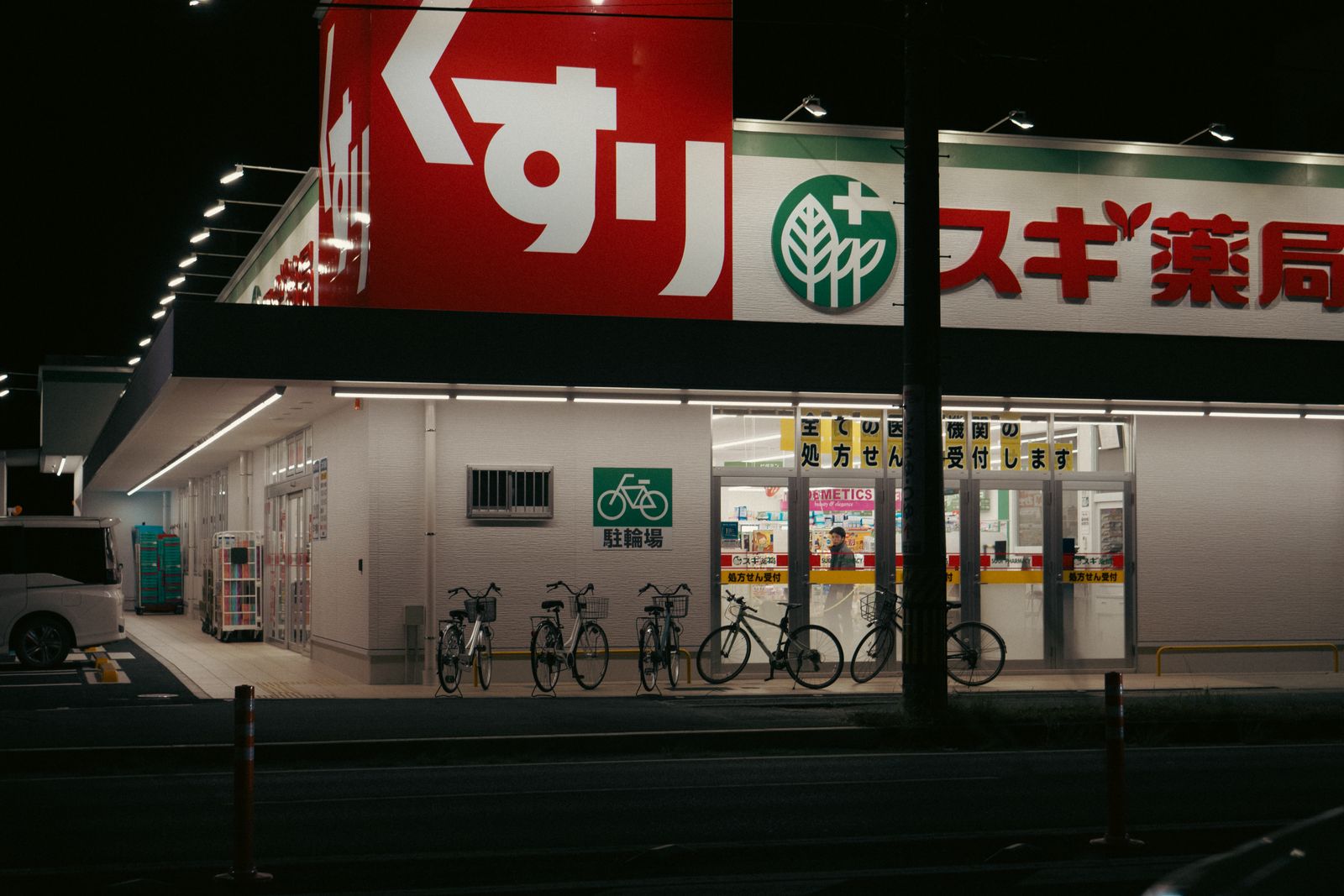 A Sugi Pharmacy at night with a large kusuri sign and yellow prescription-counter banners across the windows.