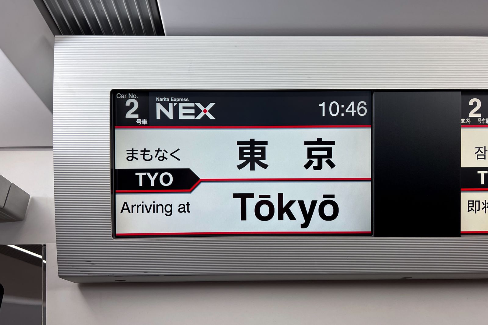 The in-car display of a Narita Express train reading Car 2, 10:46, Arriving at Tokyo, with the same notice in Japanese.
