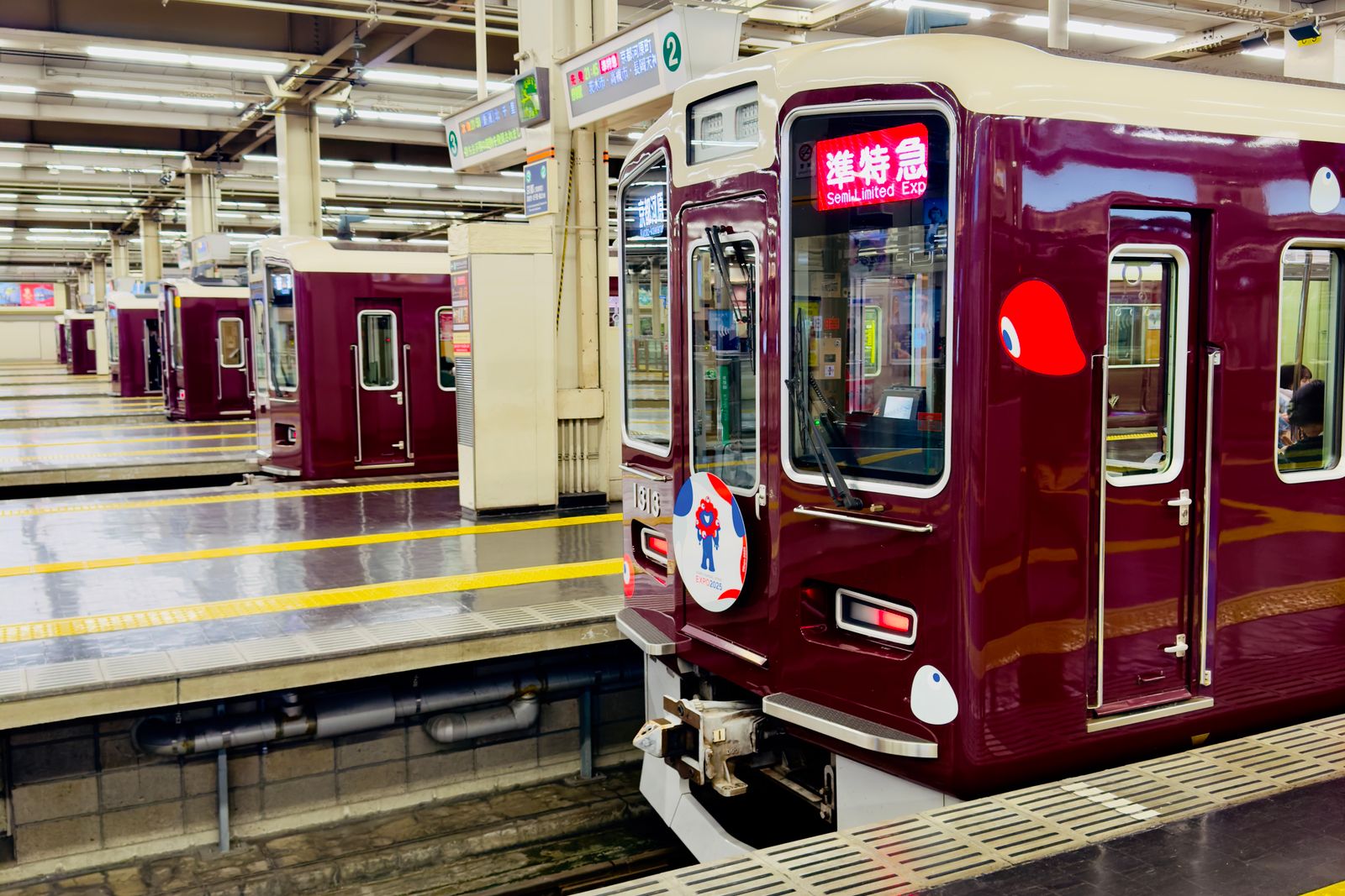 A maroon Hankyu train with a Semi Limited Express headsign at a bay platform of Osaka-Umeda station.