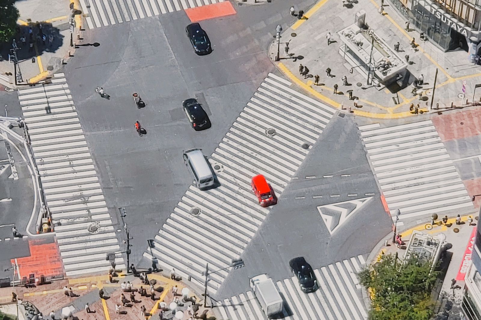 The Shibuya scramble crossing seen from directly above in daylight, small figures waiting on the corners.