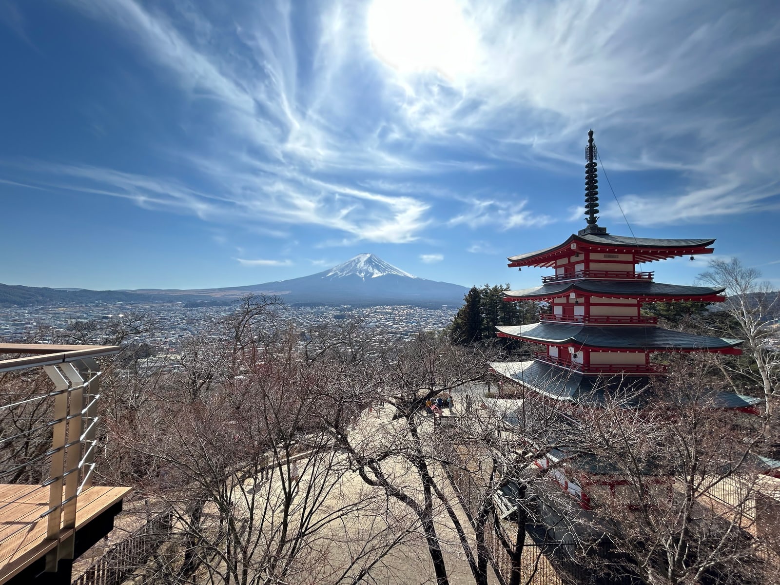 The red five-story Chureito Pagoda on a wooded slope above the town of Fujiyoshida, with a snow-capped Mount Fuji on the horizon.