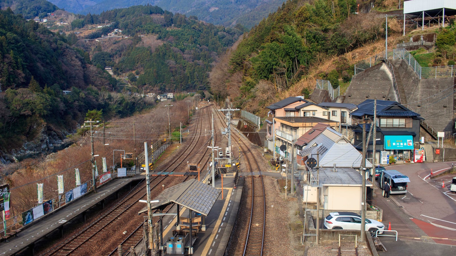 A small station with two platforms and several tracks in a narrow wooded mountain valley, with houses beside it.