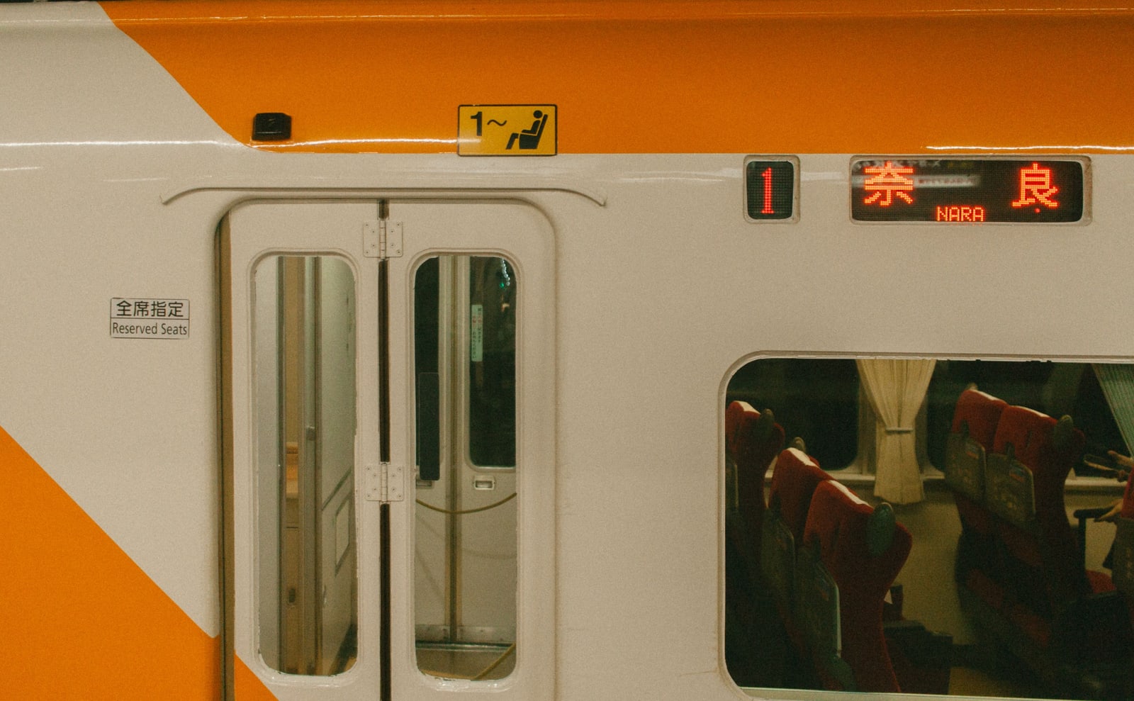 The orange and cream side of a limited-express car with a destination display reading Nara and a small plate reading all seats reserved.