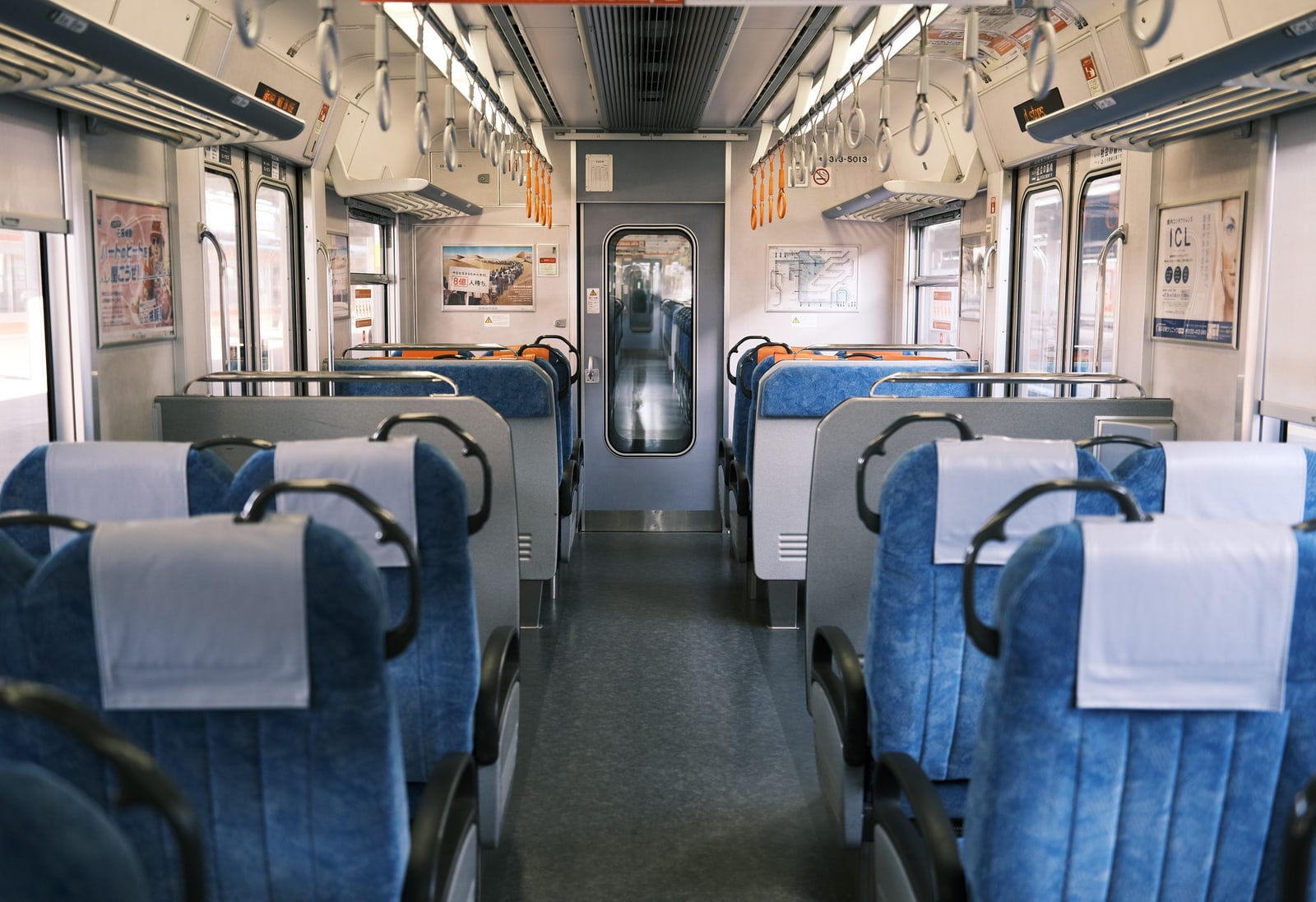 An empty Japanese local-train car with blue facing seats, white headrest covers and hanging straps.