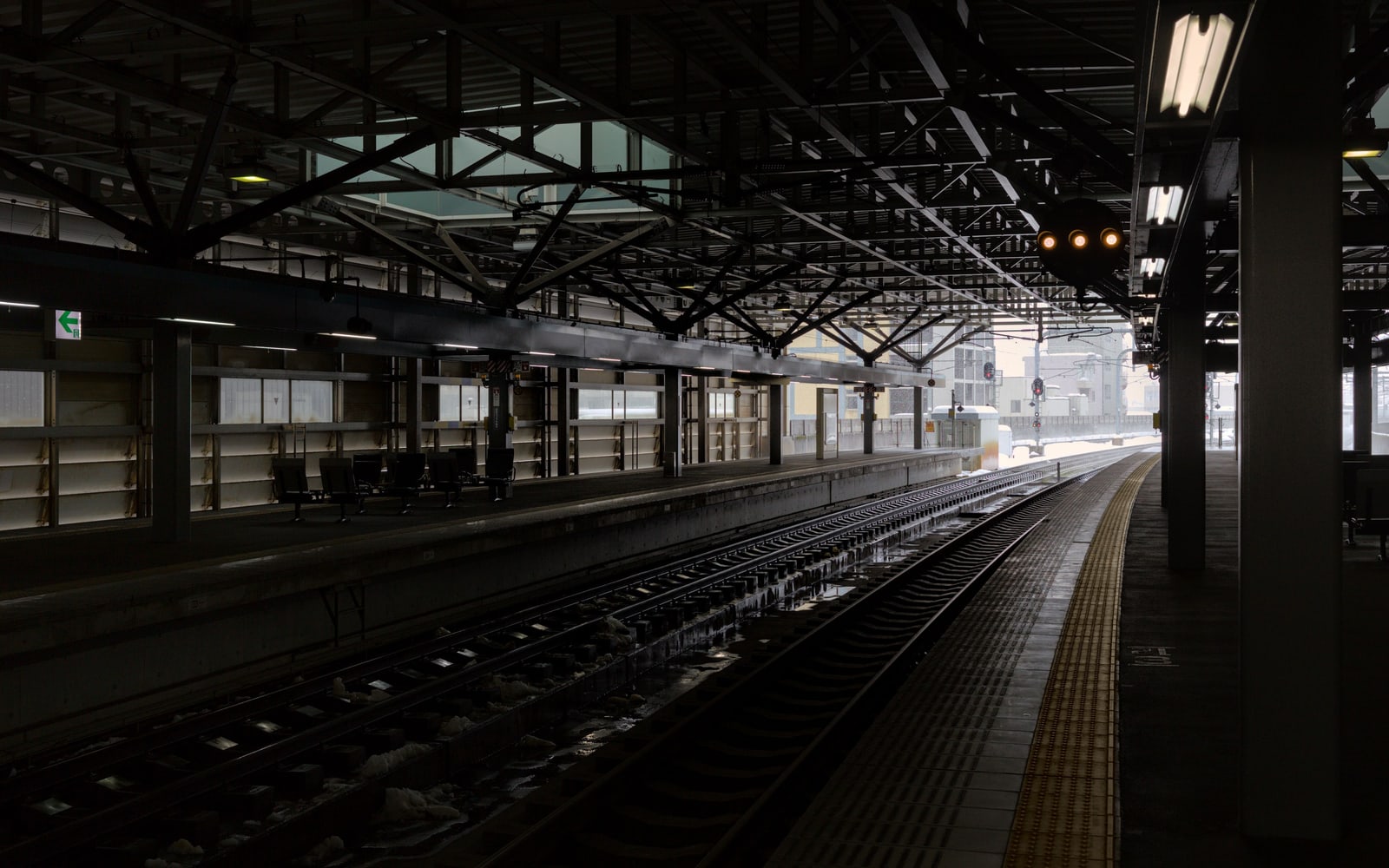 An empty railway platform under a dark steel-truss roof, with snow beside the tracks