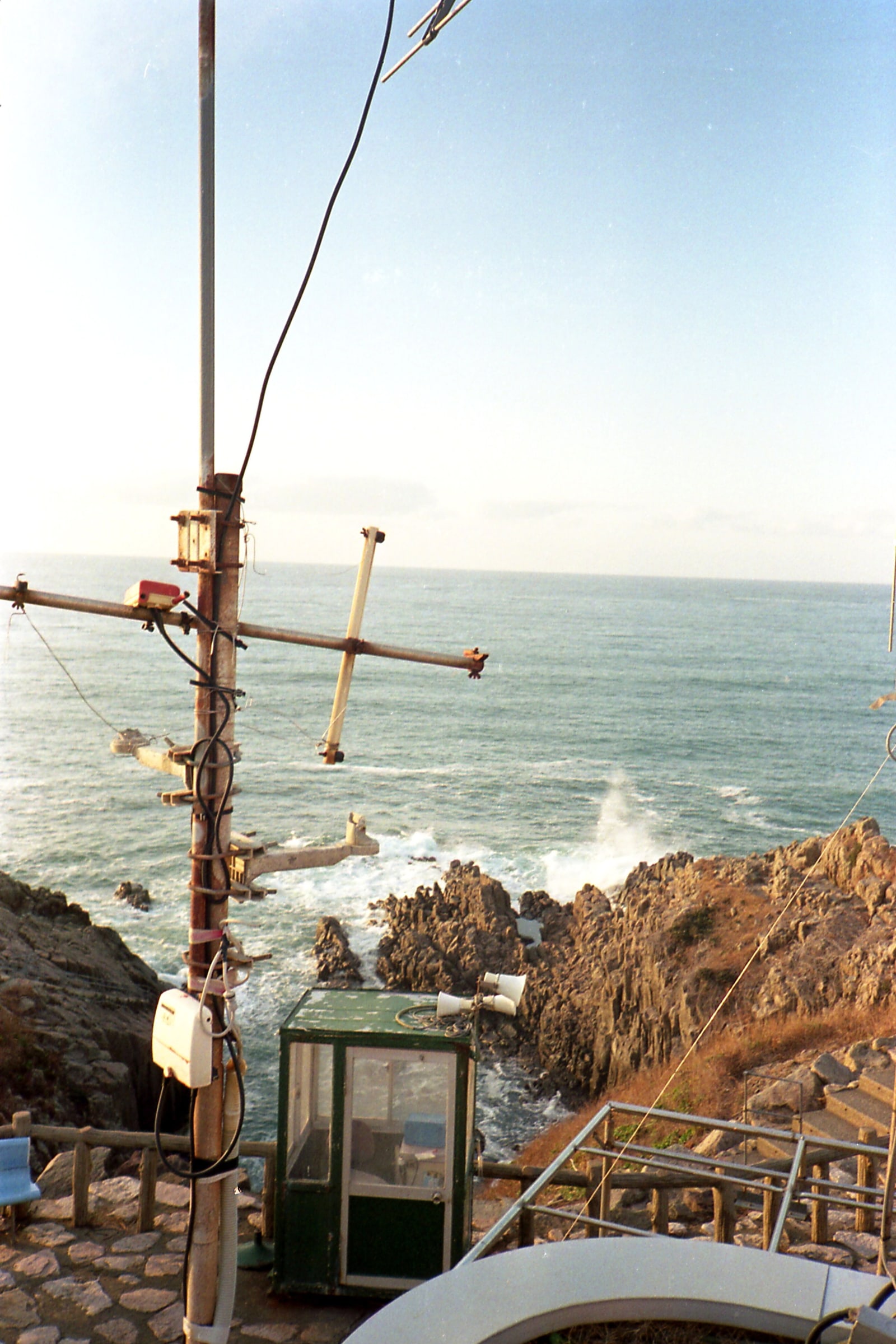 Waves breaking white on jagged brown rocks below a cliff-top terrace on the Sakai coast of Fukui, open sea to the horizon