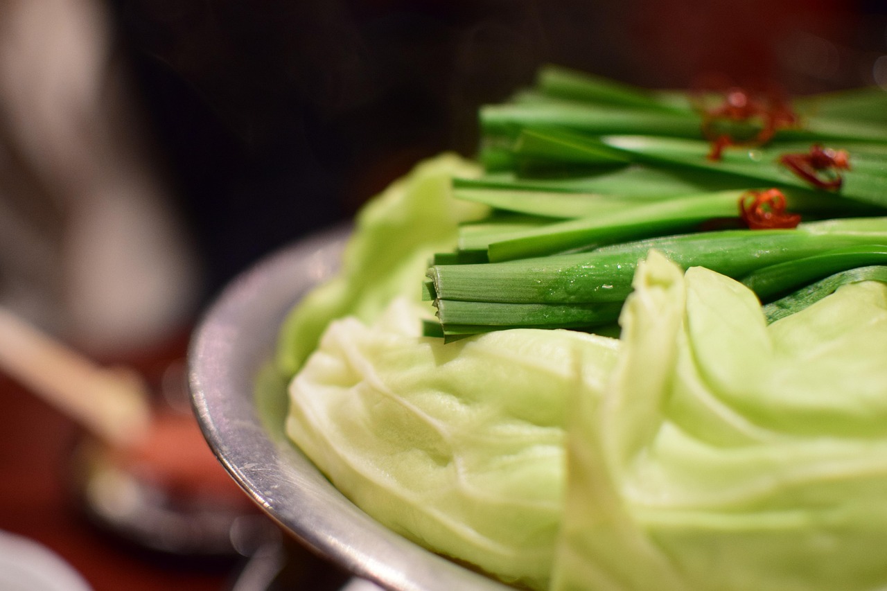 Cabbage and garlic chives stacked over a metal pot with dried chilli, steam rising — motsunabe as it arrives at the table, before it cooks down.