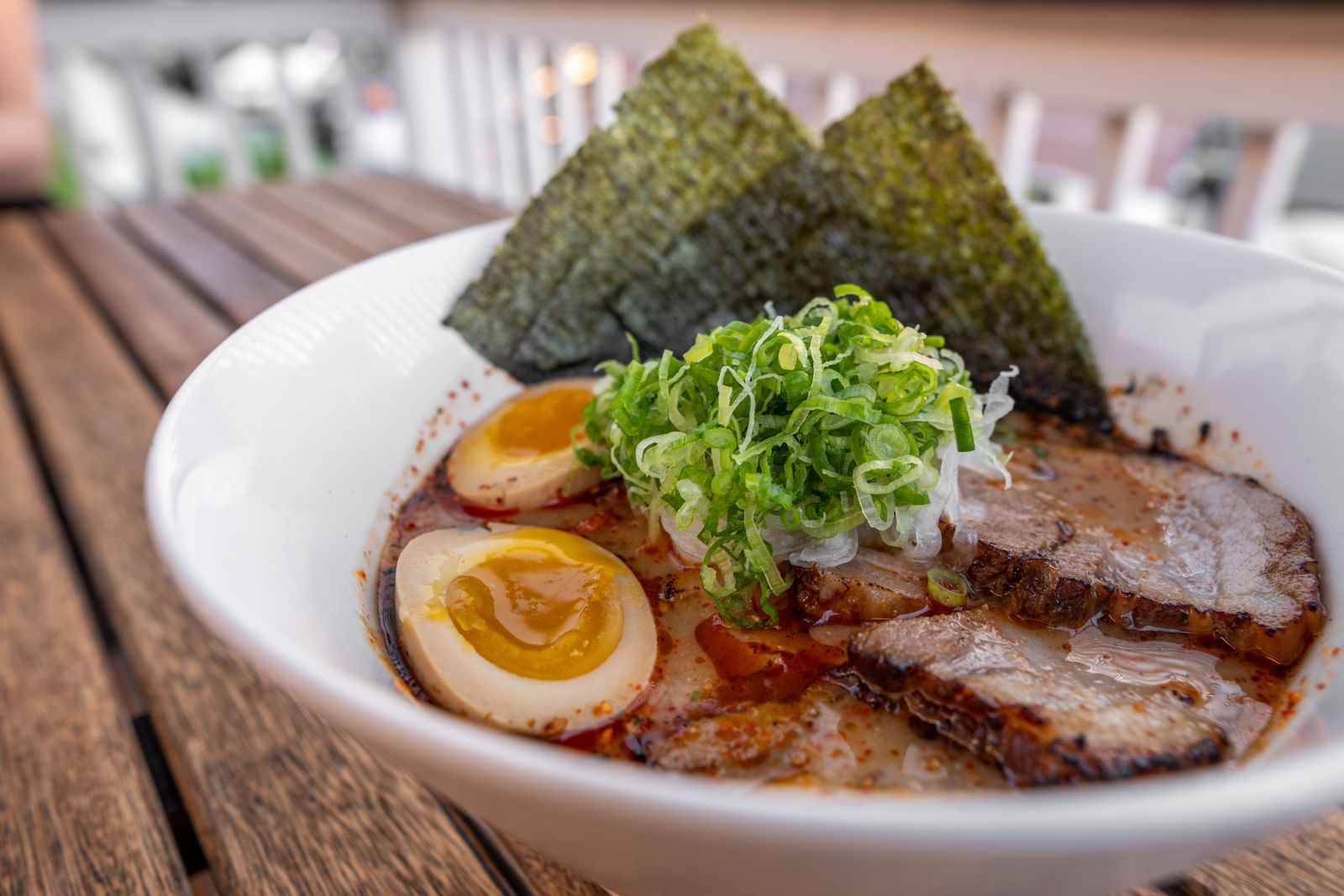 A bowl of pork-bone-broth ramen with sliced chashu, a halved marinated egg, nori and spring onion.