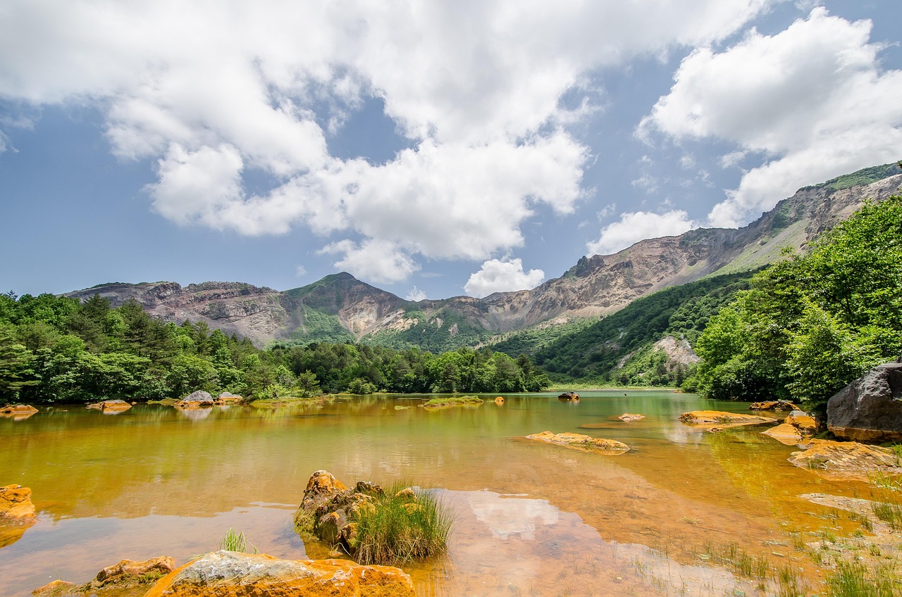 An orange-tinged shallow pond below a bare, eroded mountain ridge, green woods around