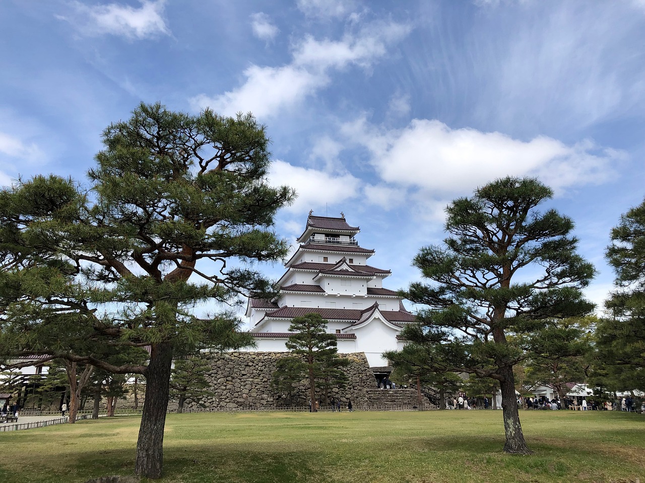 Tsurugajo in Aizu-Wakamatsu, a white keep with red-brown roof tiles on a stone base, between pines on a lawn