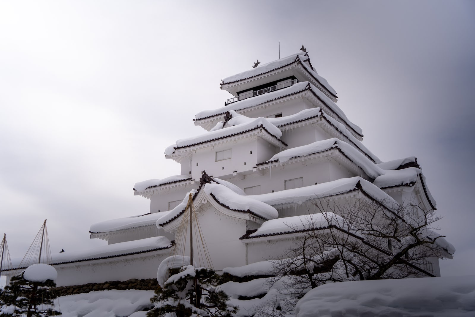 The white castle keep in Aizu-Wakamatsu under heavy snow, icicles at the eaves and snow-laden pines in front