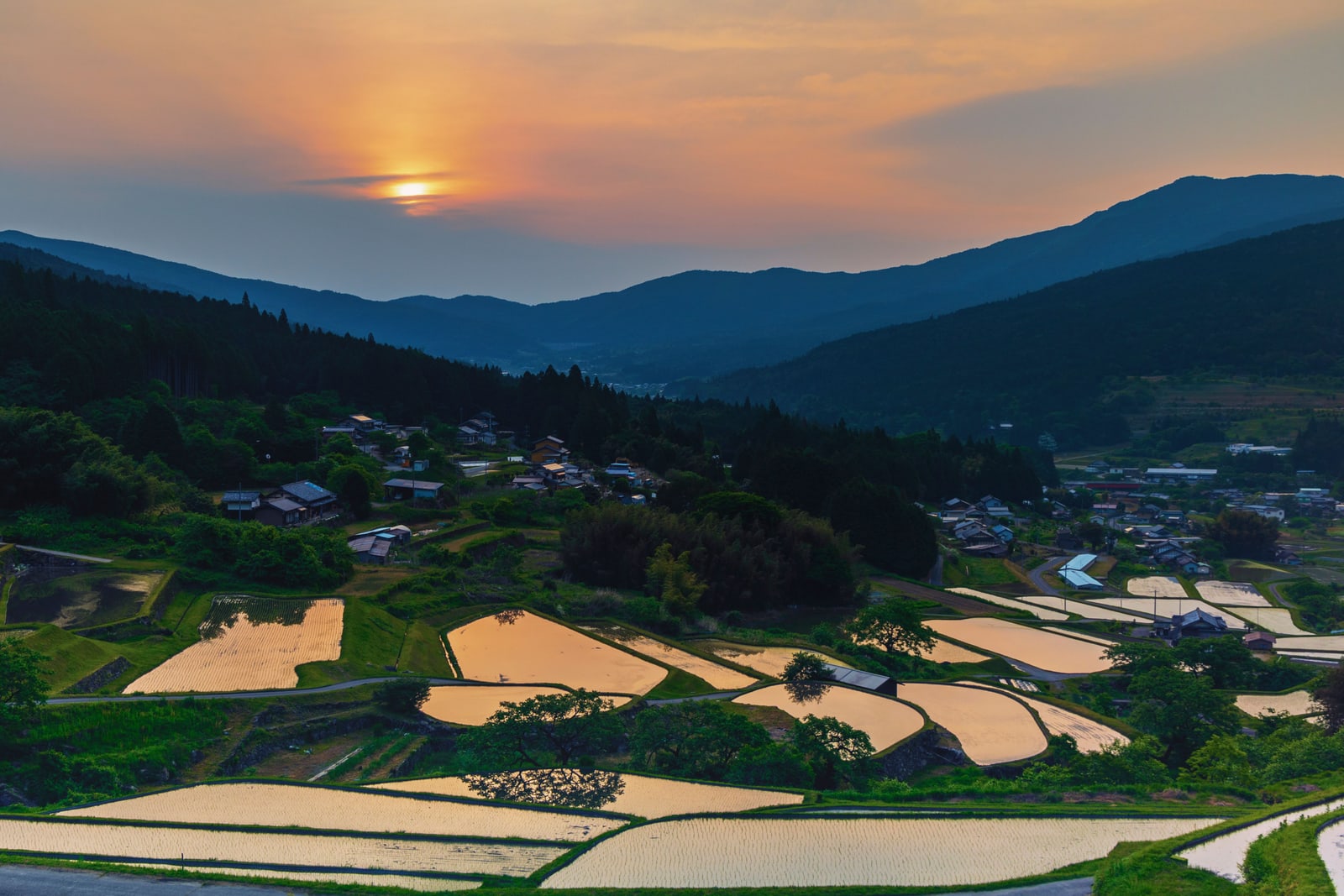 Flooded rice terraces and a hillside village at sunset in the mountains