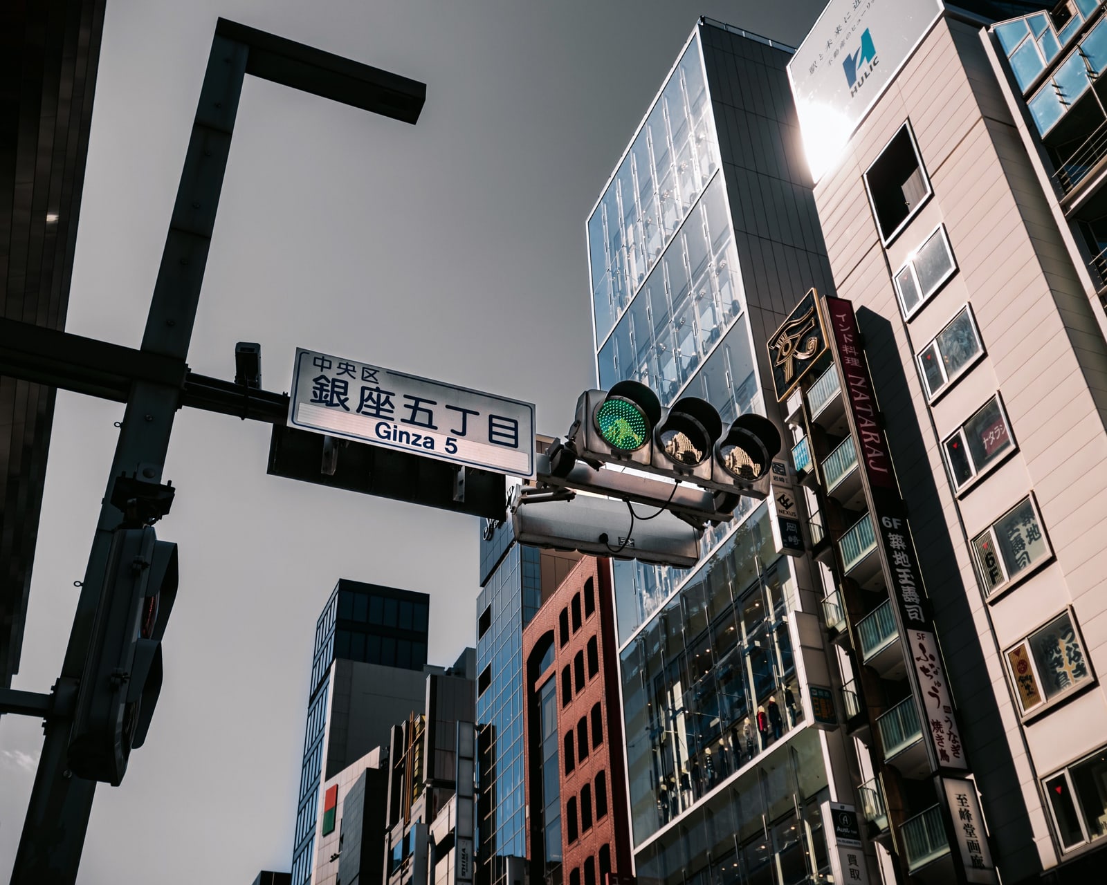 A street sign reading Ginza 5 and a traffic light, with vertical restaurant signs on a building at right
