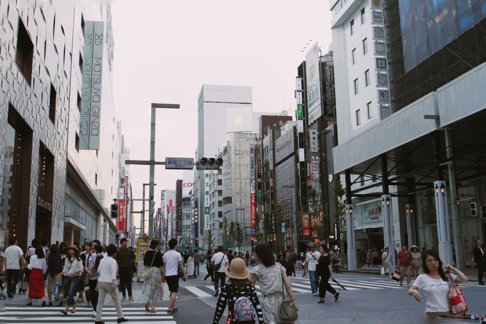 Pedestrians crossing a wide Ginza street at the Ginza 2-chome signal, department store facades on both sides and no moving vehicles