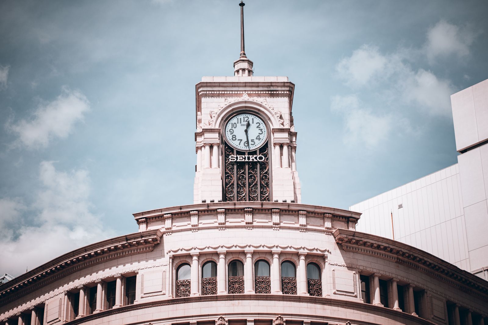 The clock tower and curved cornice of the Wako building, a white SEIKO clock face under a thin spire against a blue sky