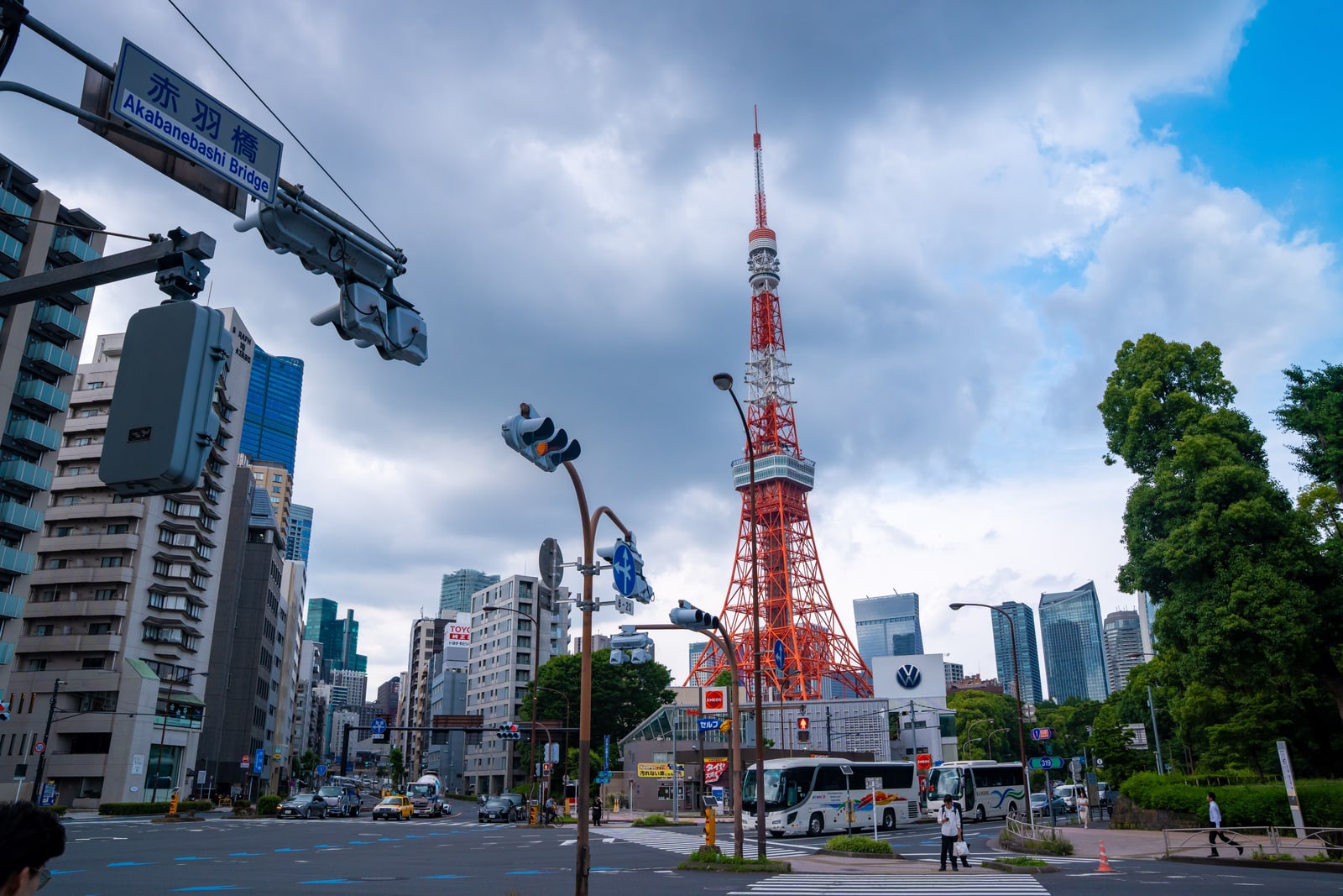 Tokyo Tower rising behind a street intersection with traffic lights and a blue Akabanebashi road sign.