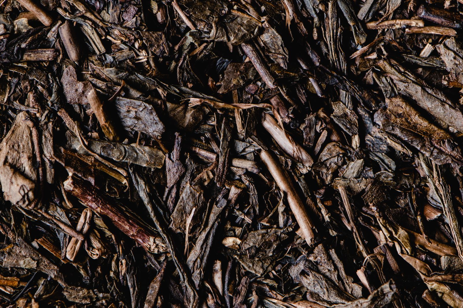 A close view of roasted tea filling the frame: flat brown leaf pieces mixed through many pale tan stem and twig fragments.