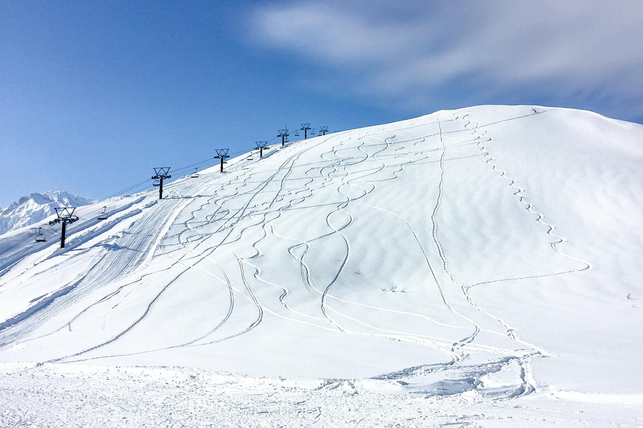 A snow slope criss-crossed with ski tracks beside a chairlift in Hakuba, under a blue sky
