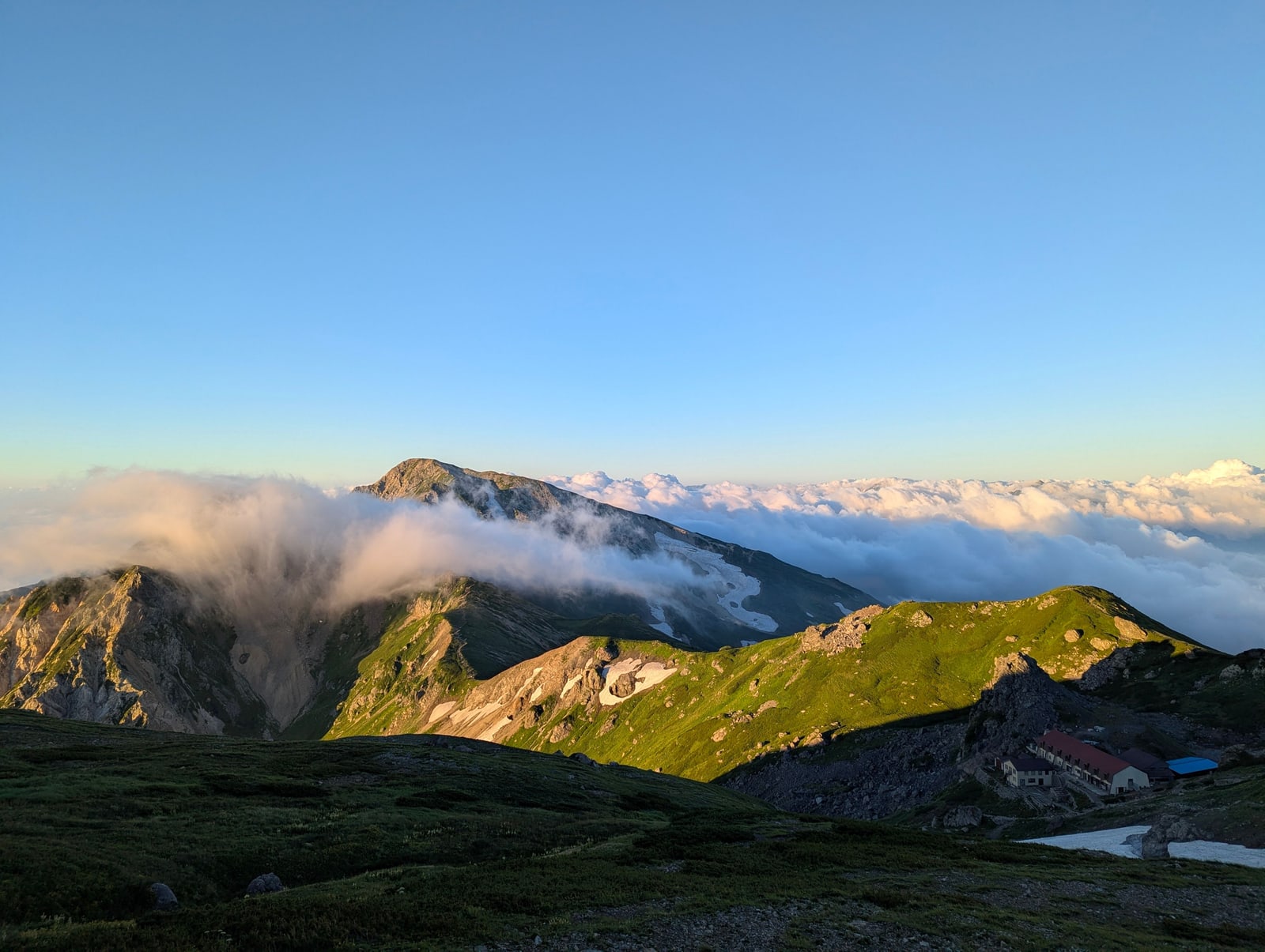 Green mountain ridges above a sea of cloud in early light, mountain huts below, Hakuba area