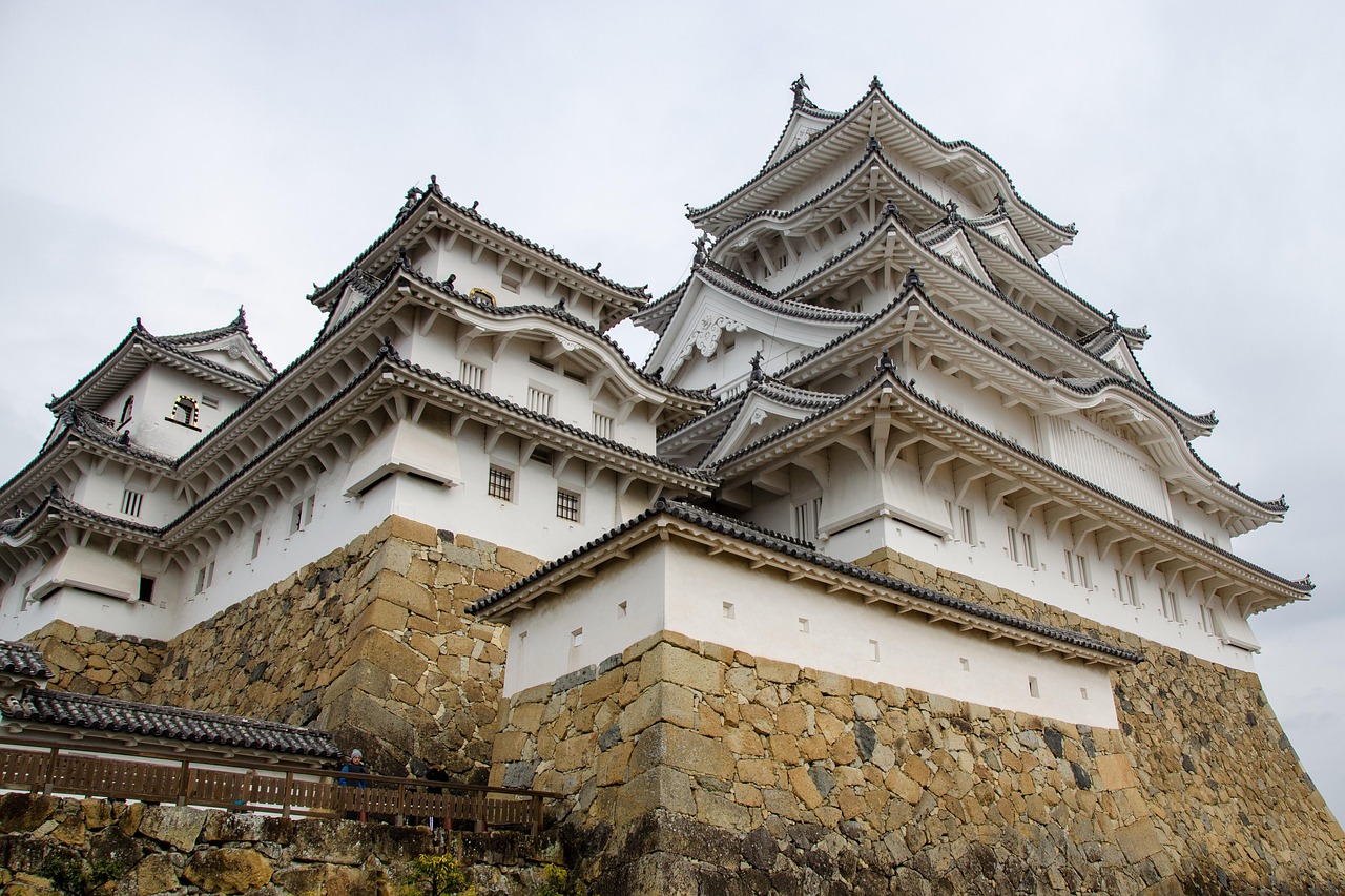 The keep and its connected turrets seen from below, layered gray tile roofs and white walls on a high stone base.