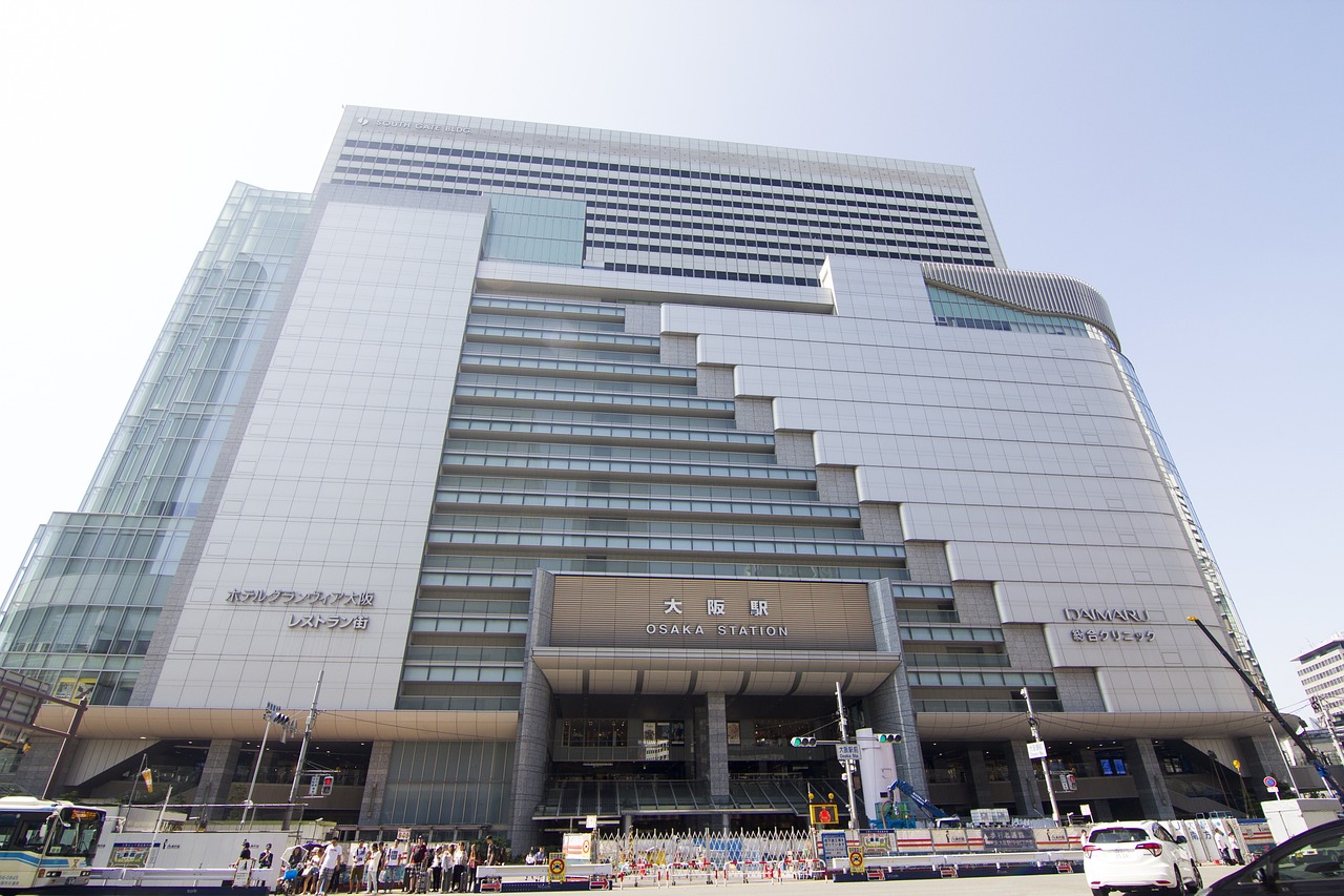 A tall gray station building with the sign Osaka Station above its entrance, small figures at street level.